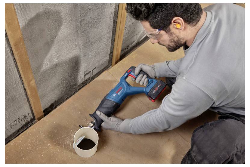 Ein Bauarbeiter mit Schutzbrille und Maske benutzt eine Säbelsäge, um Holzrahmen in einem Haus im Bau zu schneiden.