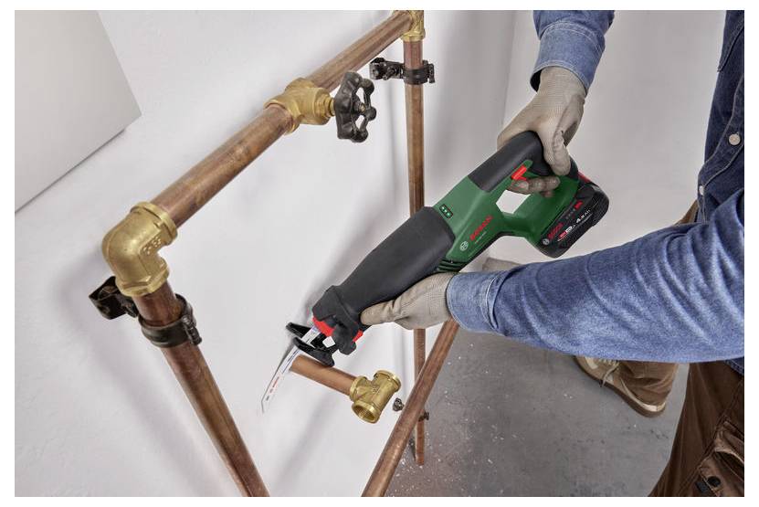 Eine Person benutzt eine grüne Reciprosäge, um ein Kupferrohr in einer Sanitärreparaturinstallation zu schneiden.