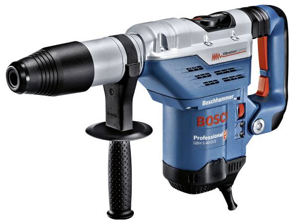 Arbeiter kniet in einem Technikraum und bohrt mit einer Elektrobohrmaschine, um ein Rohr neben offenliegenden Rohrleitungen zu schneiden oder zu installieren.