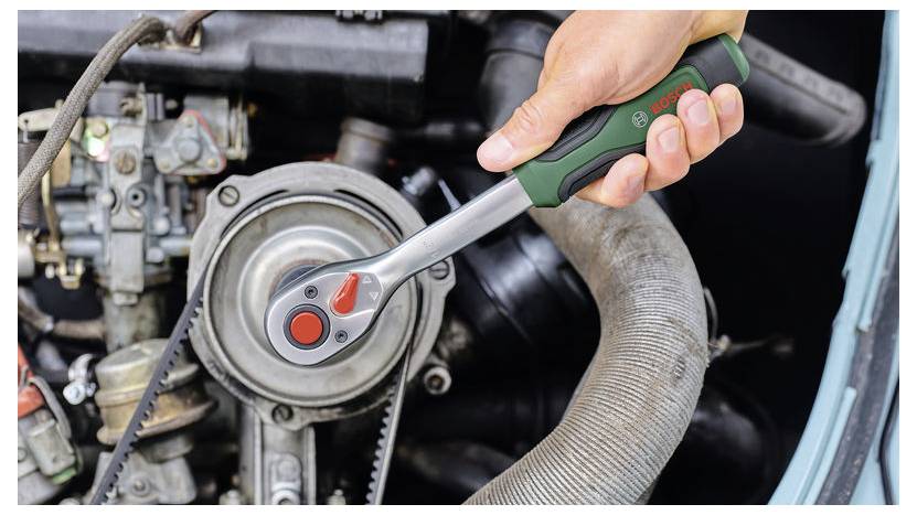 Nahaufnahme einer Hand, die einen Bosch-Ratschenschlüssel verwendet, um eine Motorkomponente in einem Motorraum eines Autos festzuziehen oder zu lockern.