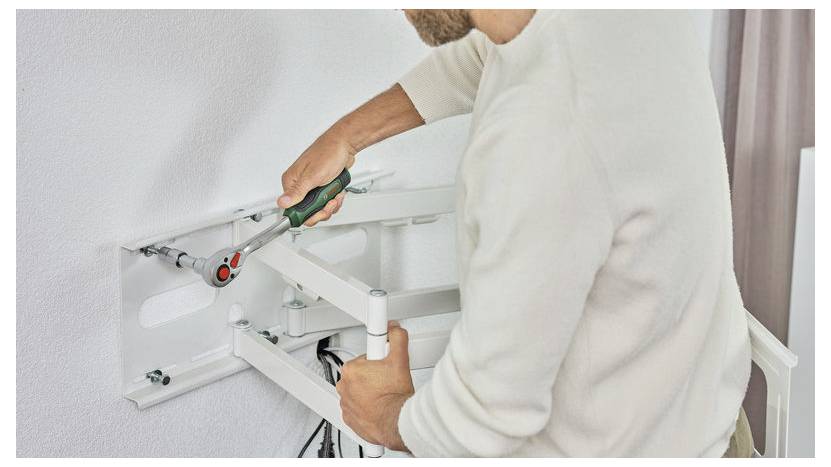 Person beim Montieren oder Anpassen eines weißen, an der Wand befestigten Klappttisches mit einem Schraubenschlüssel in einem Wohnungsinterieur.