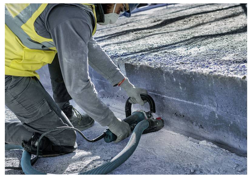Arbeiter in Schutzausrüstung, der ein Handwerkzeug verwendet, um Eis an einer Bordsteinkante oder Straßenrand im Freien zu schneiden oder zu schleifen.