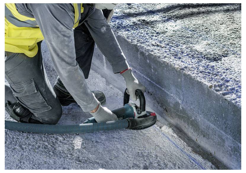 Arbeiter, der mit einer tragbaren Betonschneidsäge entlang der Kante eines Bordsteins oder einer Betonplatte schneidet, mit angeschlossener Staubschlauch.