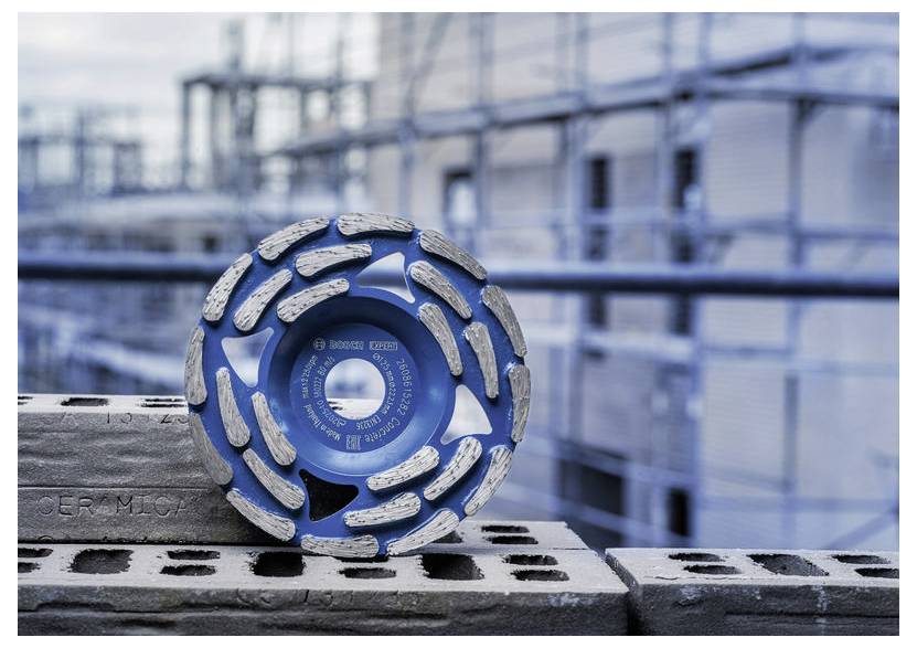 Schleifrad mit blauem Diamantbelag ruht auf Betonblöcken auf einer Baustelle, mit unscharfem Baugerüst im Hintergrund.