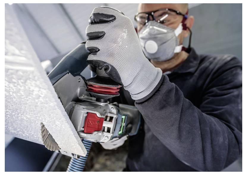 Arbeiter mit Handschuhen, Schutzbrille und Atemschutzmaske, der einen Elektroschleiffer auf einer Metalloberfläche verwendet.