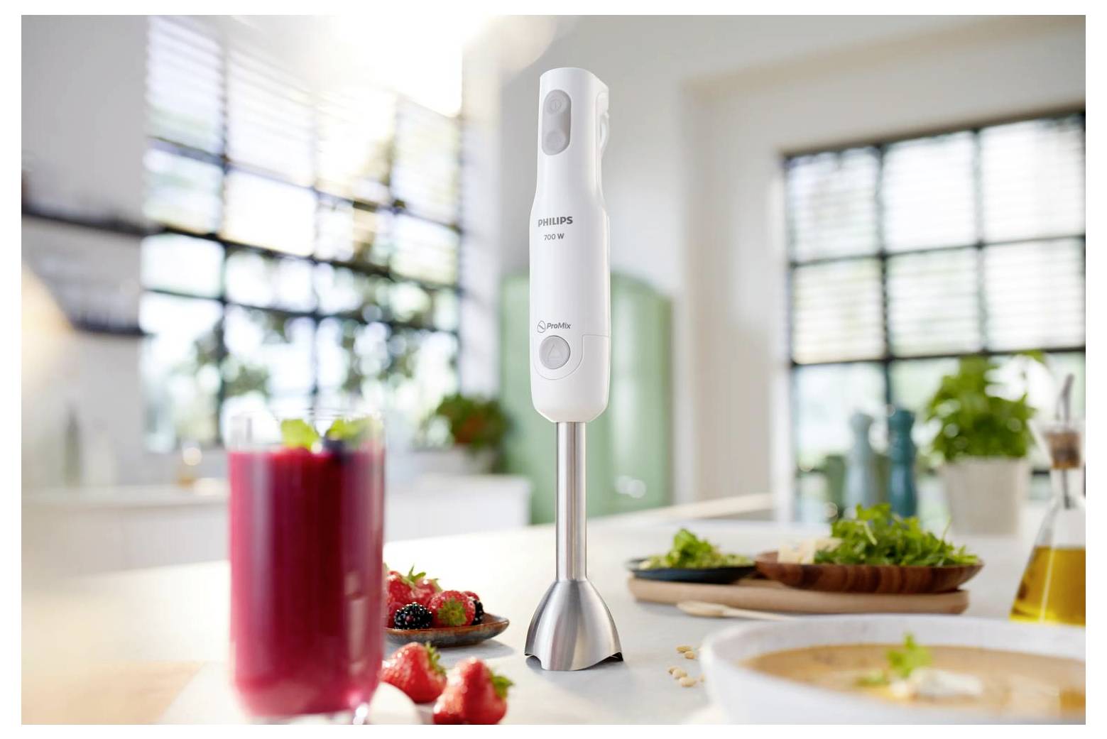 Philips Stabmixer steht auf einer Küchenablage neben einem roten Smoothie und vorbereiteten Zutaten in einer hellen Heimatküche.