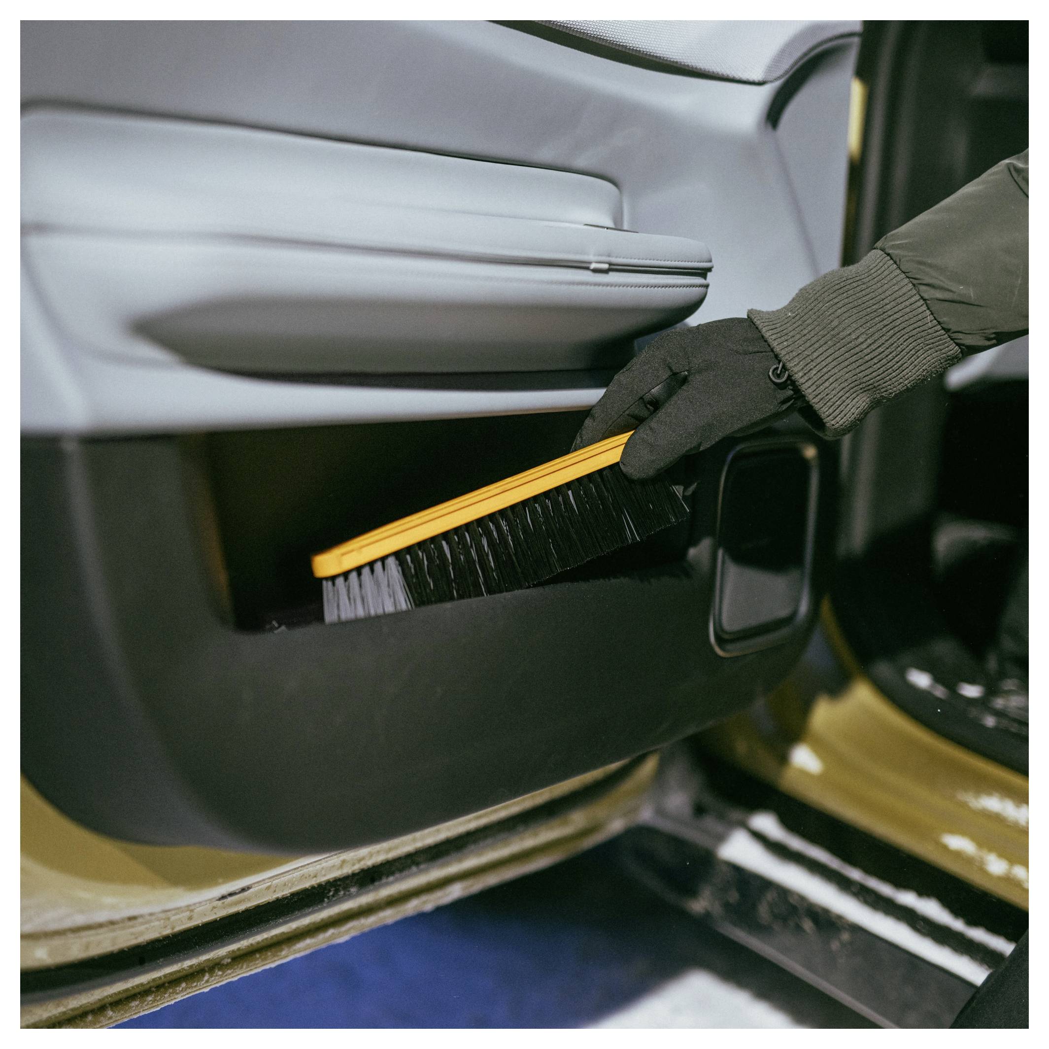 Behandschuhte Hand verwendet eine Bürste, um Staub von der unteren Innenseite einer Autotür zu reinigen.