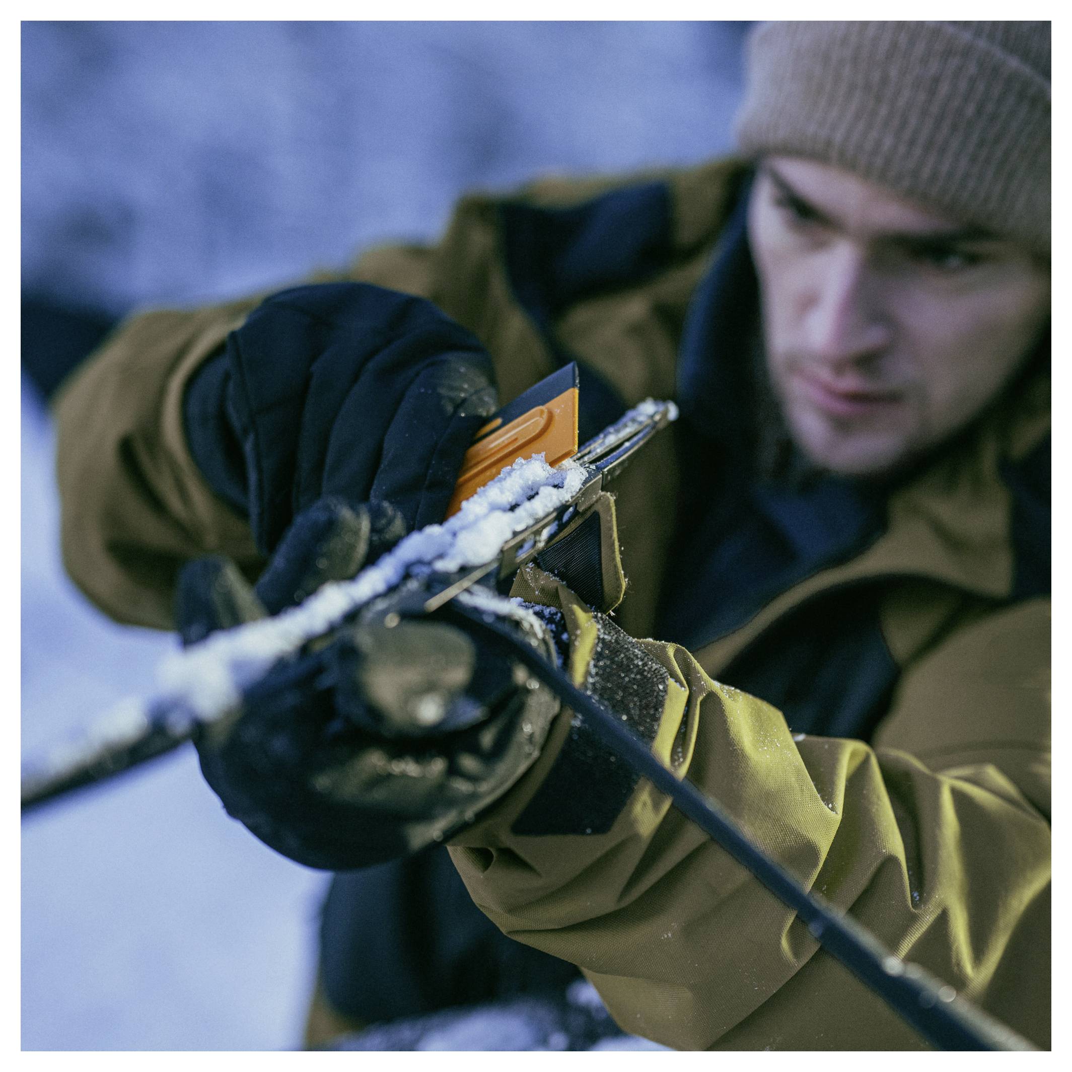 Nahaufnahme eines Mannes in Winterkleidung, der draußen Schnee von einem Gewehr entfernt.