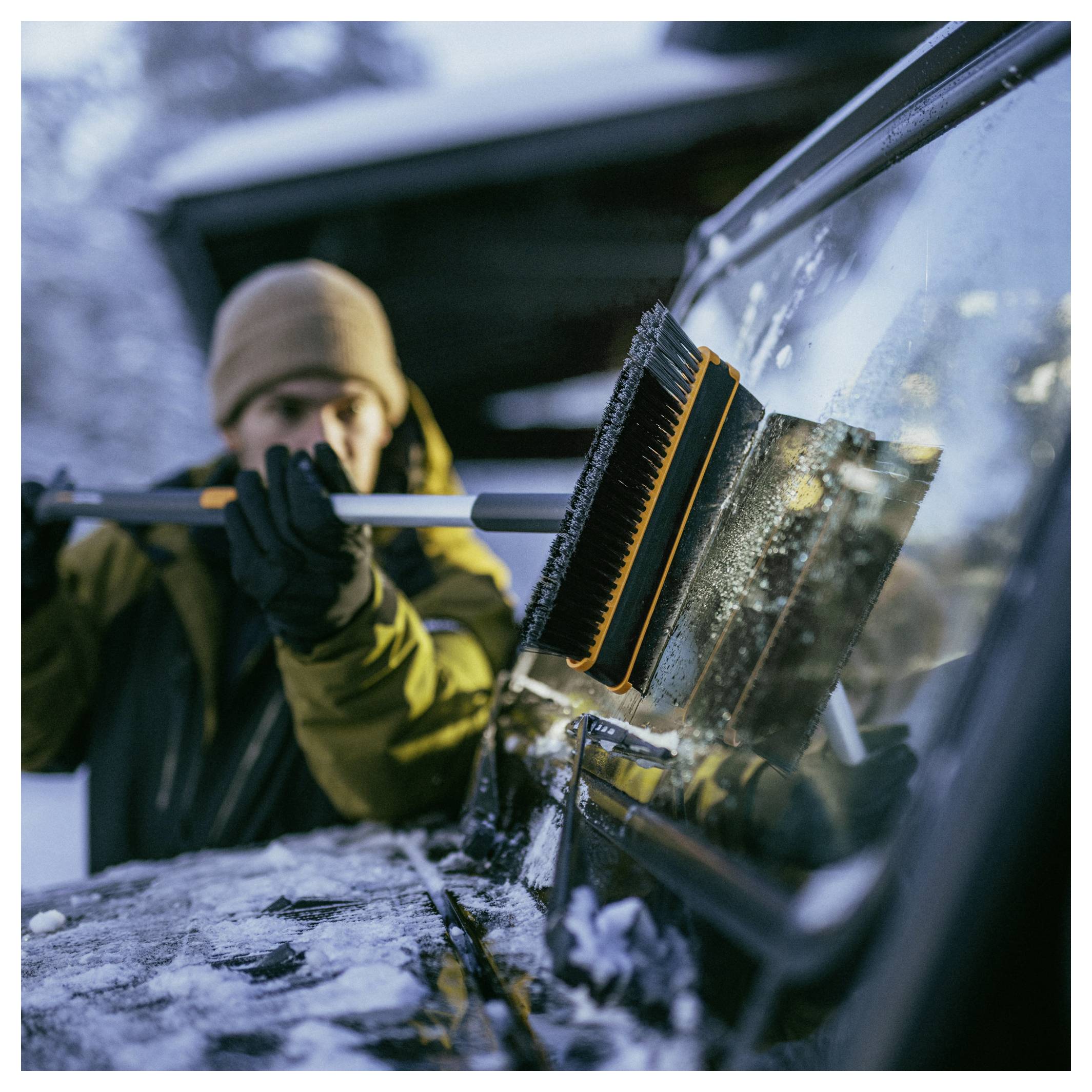 Eine Person, die mit einem Besen Schnee und Eis von einer Autoscheibe im Winter entfernt.