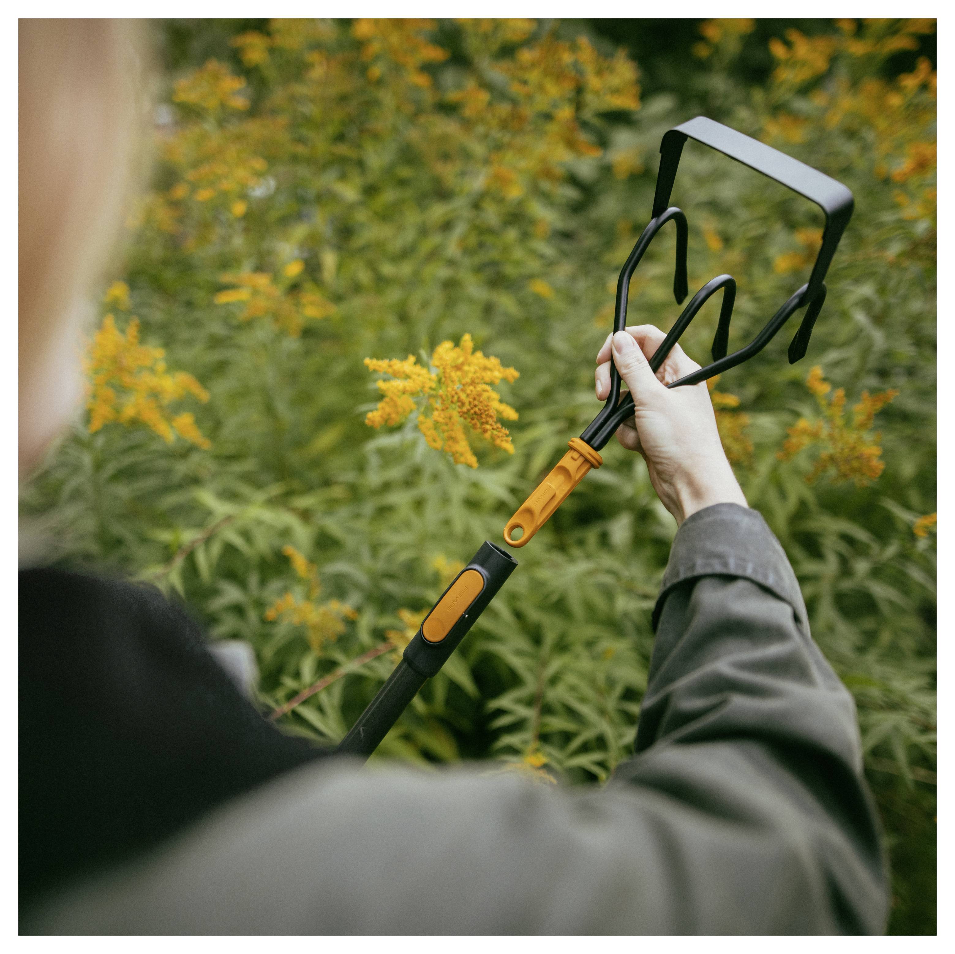 Person, die ein Gartenwerkzeug verwendet, um gelbe Blumen in einem blattreichen Außengarten zu schneiden