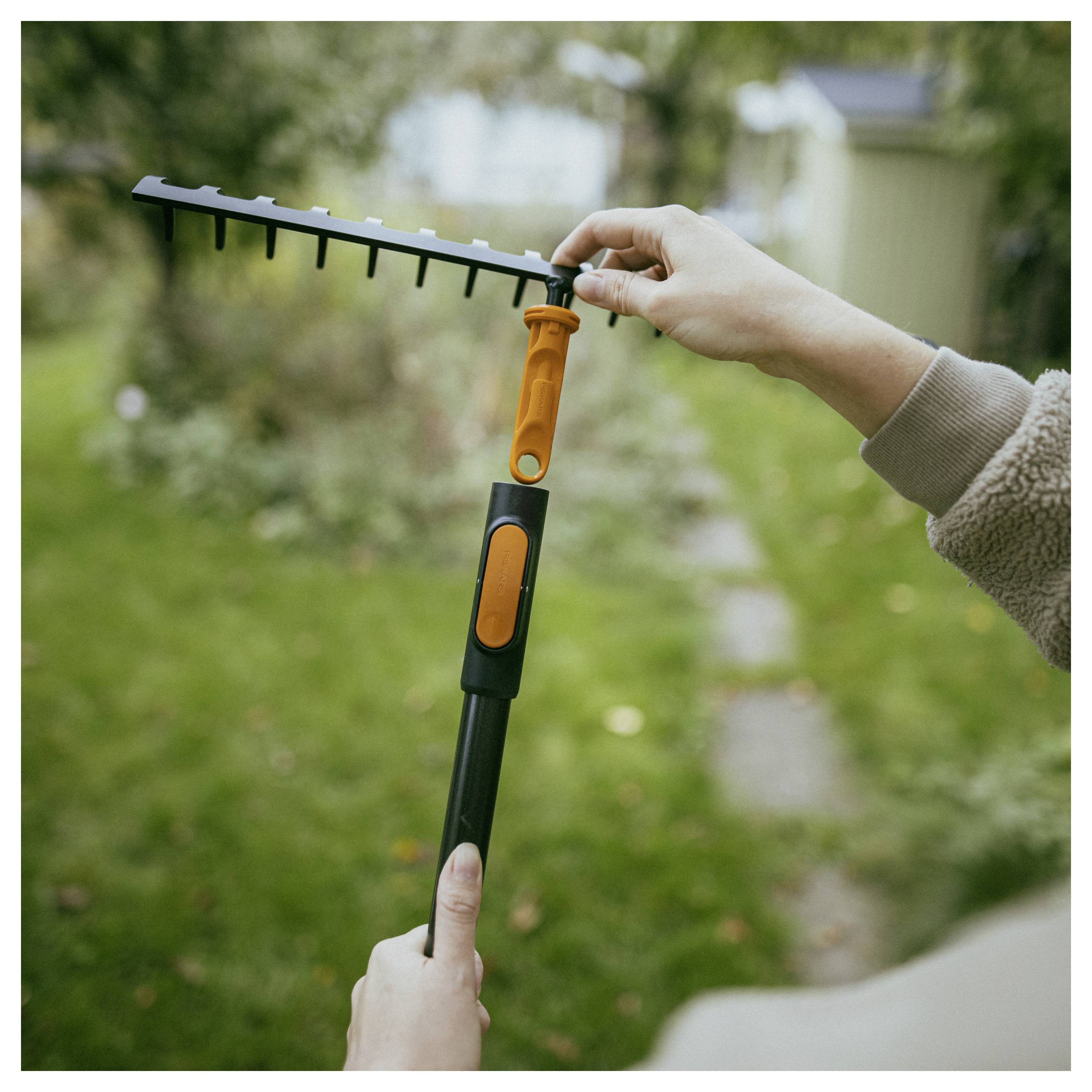 Person hält einen ausziehbaren Gartenrechen oder ein Laubkamm im Freien in einem Garten und stellt ihn ein.