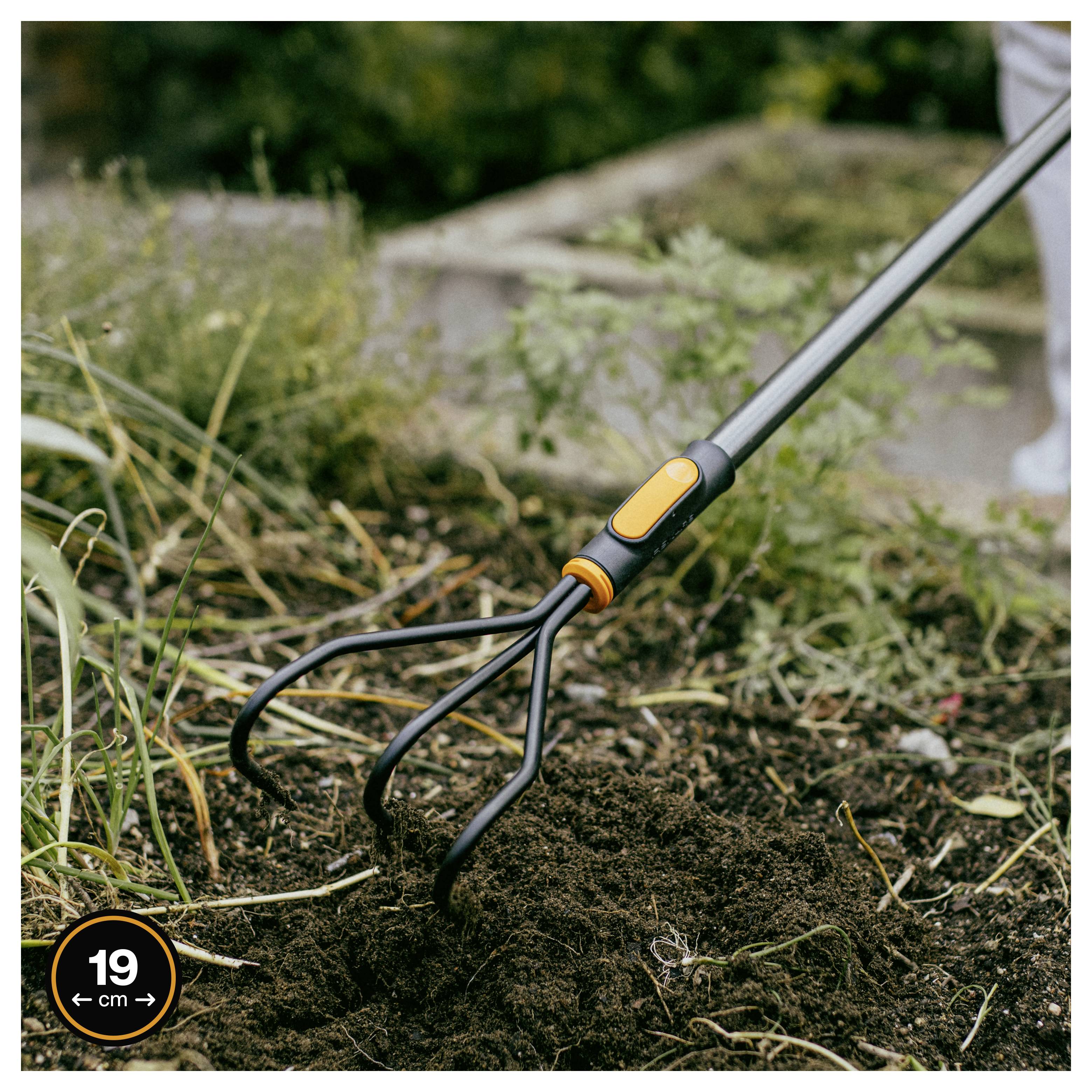 Gartenkultivator lockert Erde in einem Gartenbeet auf, gezeigt mit einem 19 cm Breitenindikator.