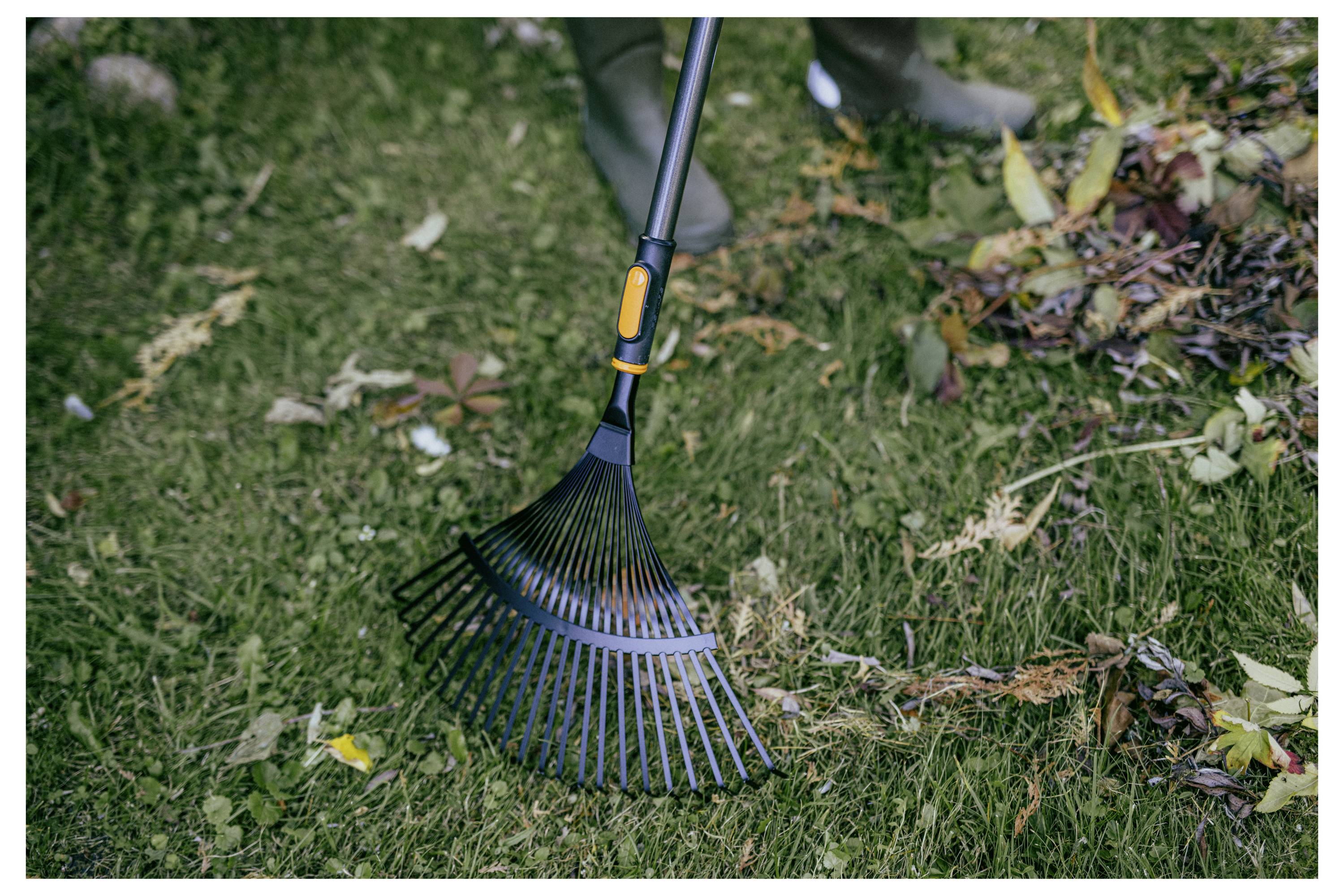 Eine Person verwendet einen breiten Gartenrechen, um herabgefallene Blätter von einem grasbewachsenen Rasen zu sammeln.