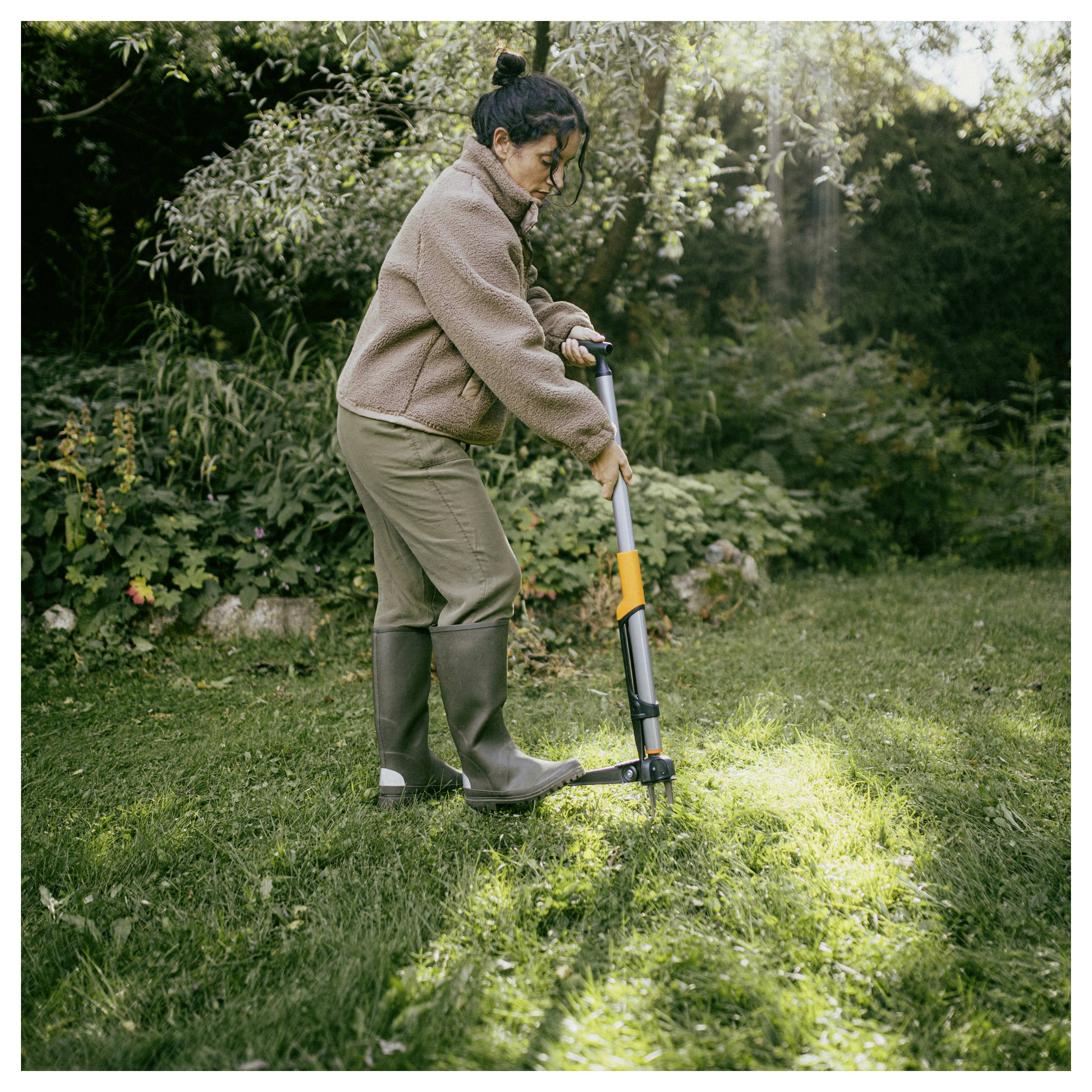 Frau, die einen manuellen Rasenmäher benutzt, um einen sonnigen Rasen in einem Garten zu trimmen.