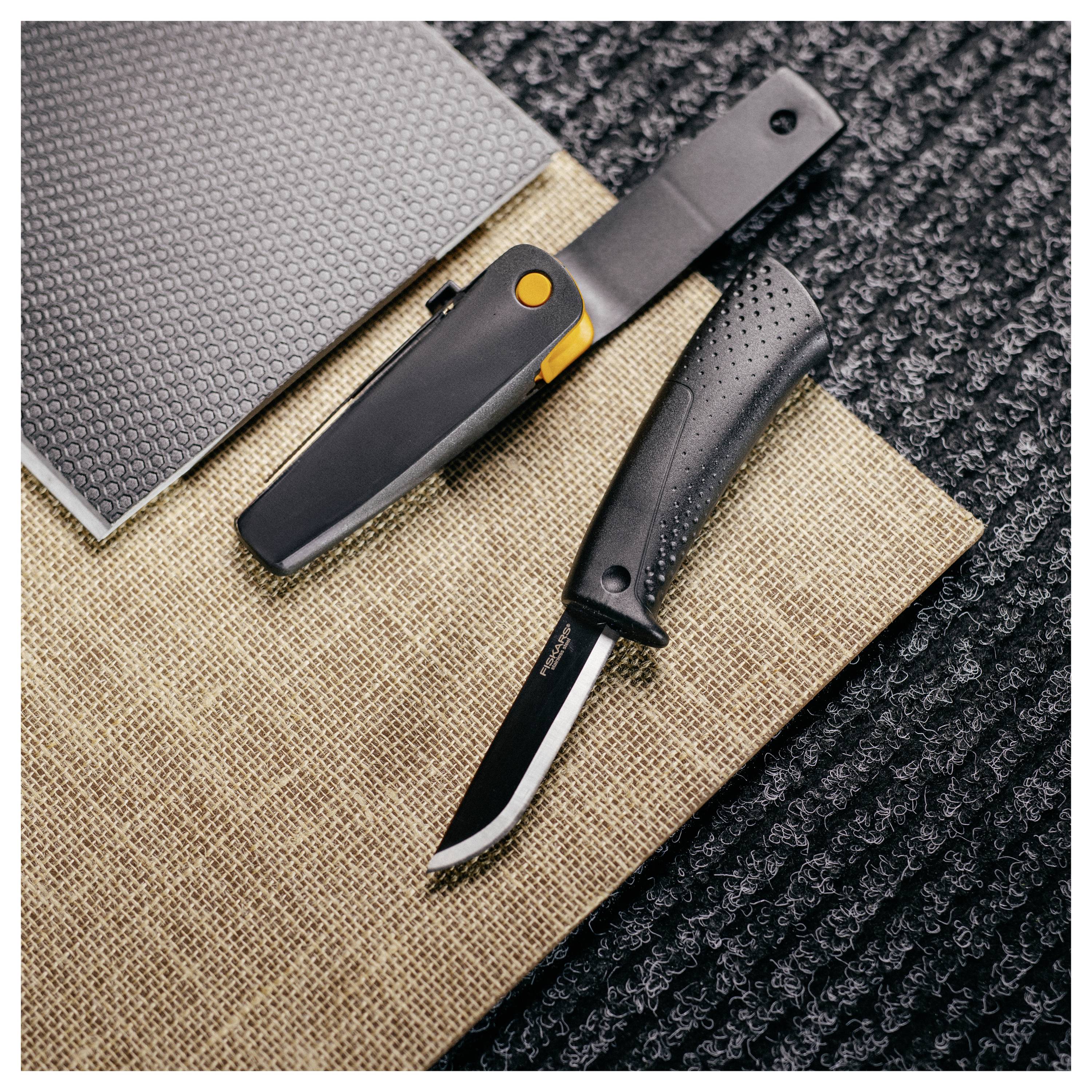 Zwei schwarze Messer mit feststehender Klinge und strukturierten Griffen sind diagonal auf überlappenden Stoff-Musterproben in Grau, Beige und Schwarz angeordnet.