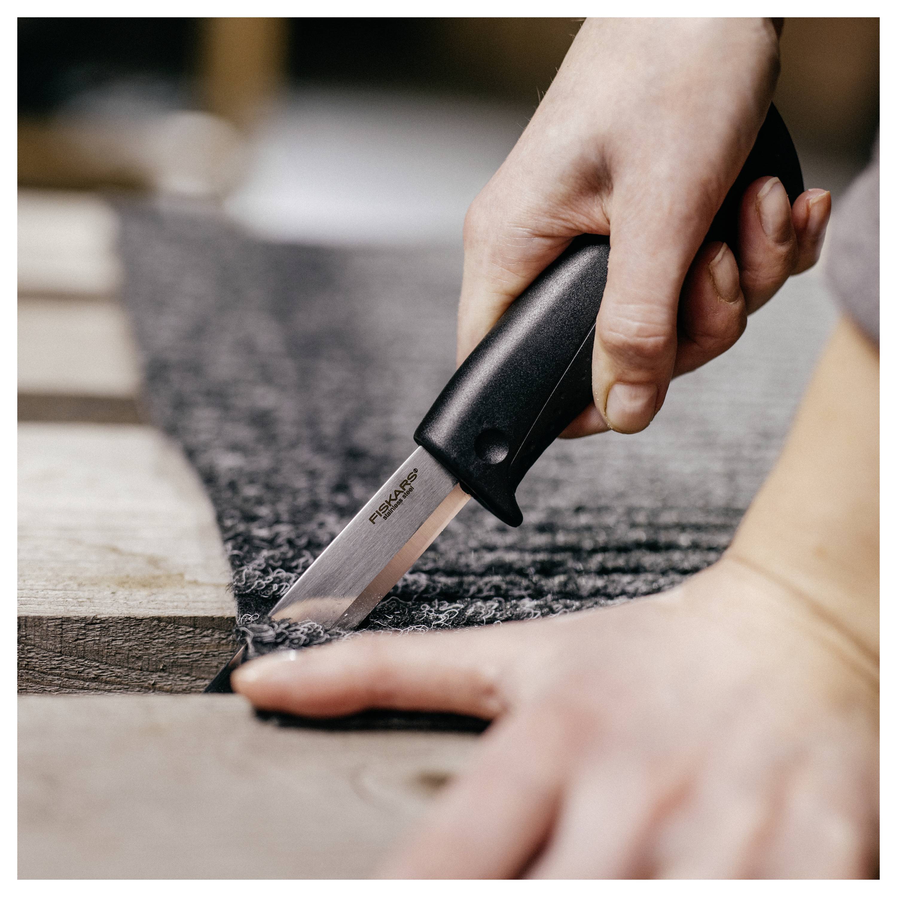 Nahaufnahme einer Hand, die mit einem Universalmesser Teppich oder Stoff auf einem Holzboden schneidet.