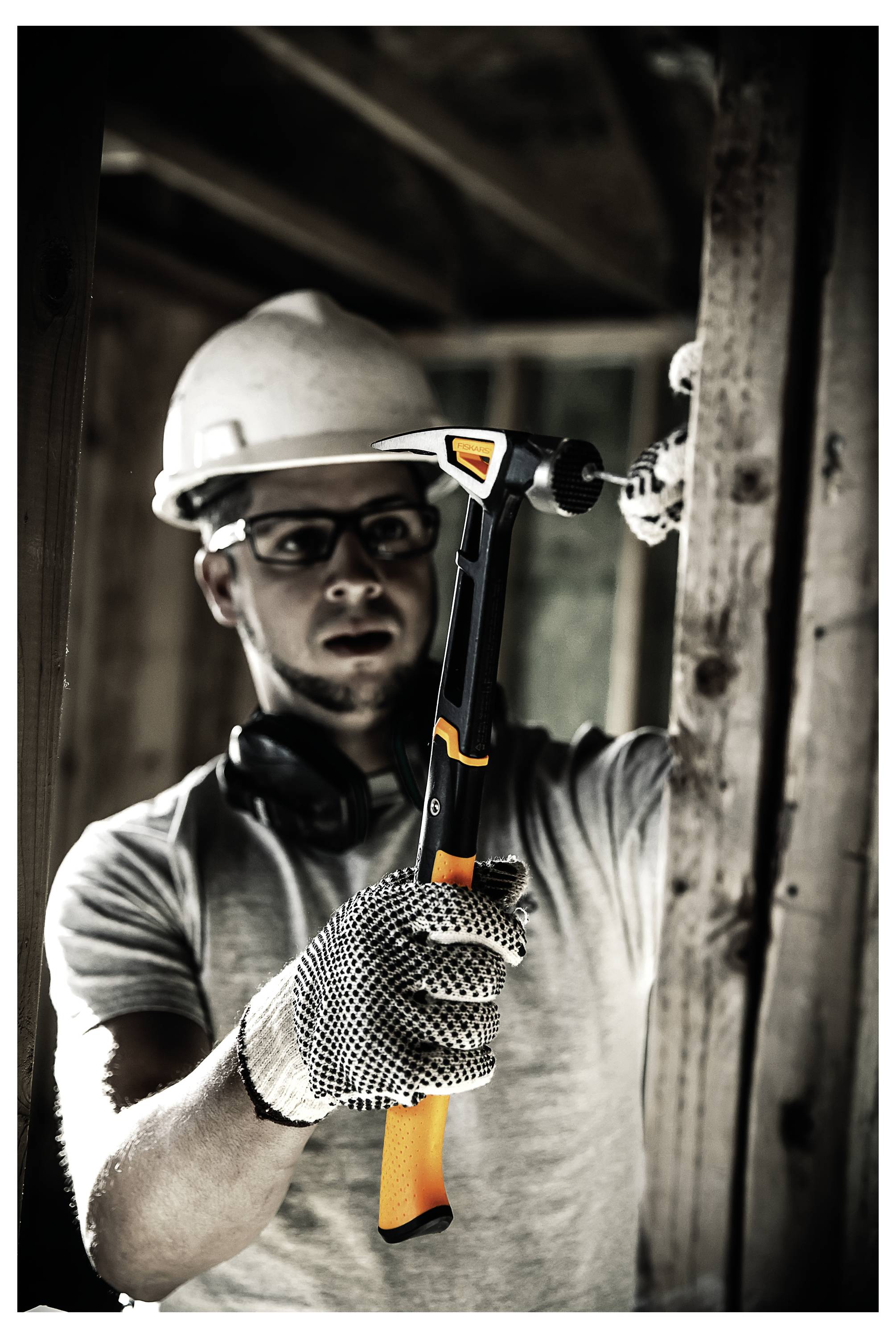 Bauarbeiter mit Schutzhelm und Handschuhen, der einen Hammer hält und in einem Gebäuderahmen arbeitet.