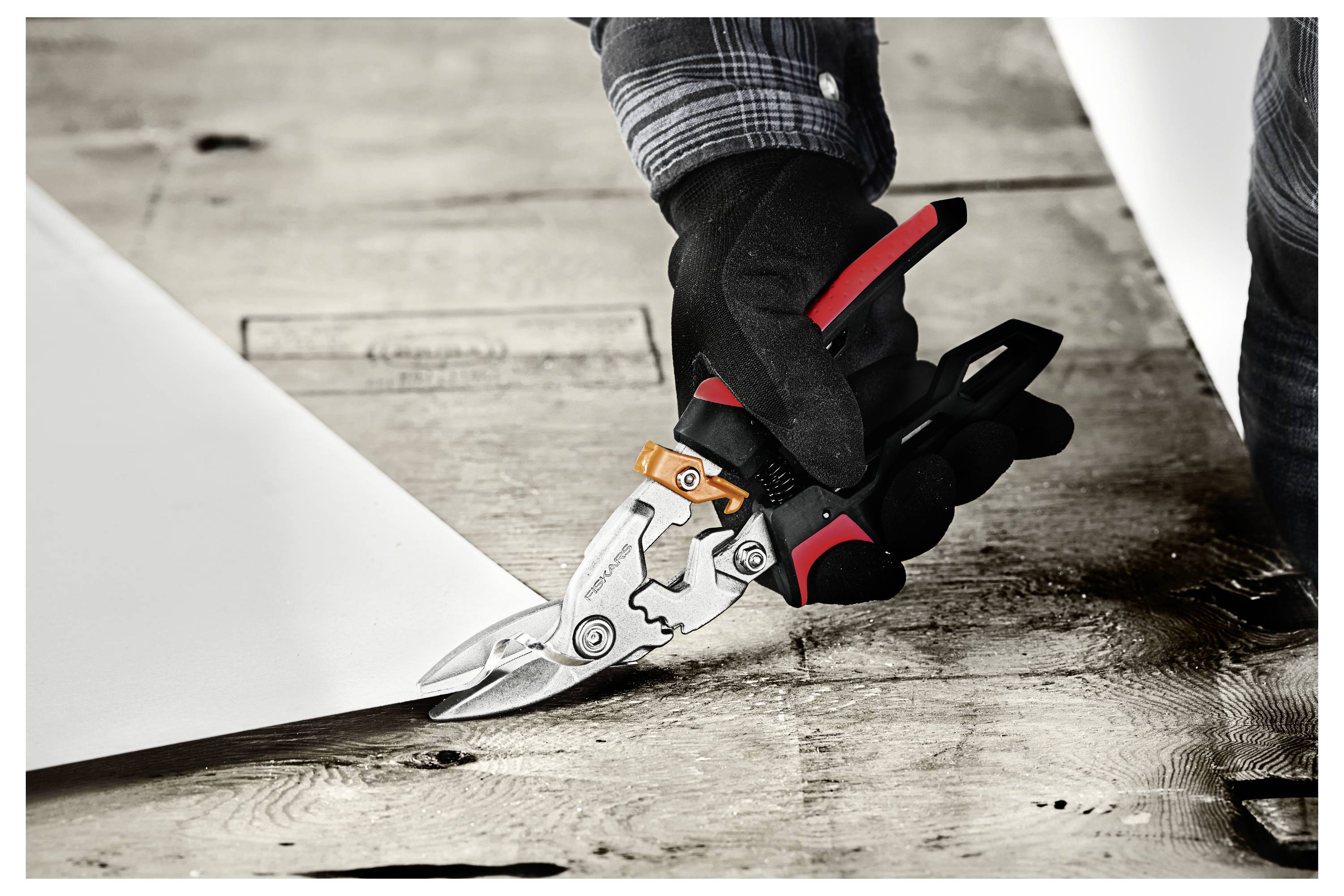 Behandschuhte Hand, die mit einer Metallschere ein weißes Blatt auf einer Werkbank schneidet.