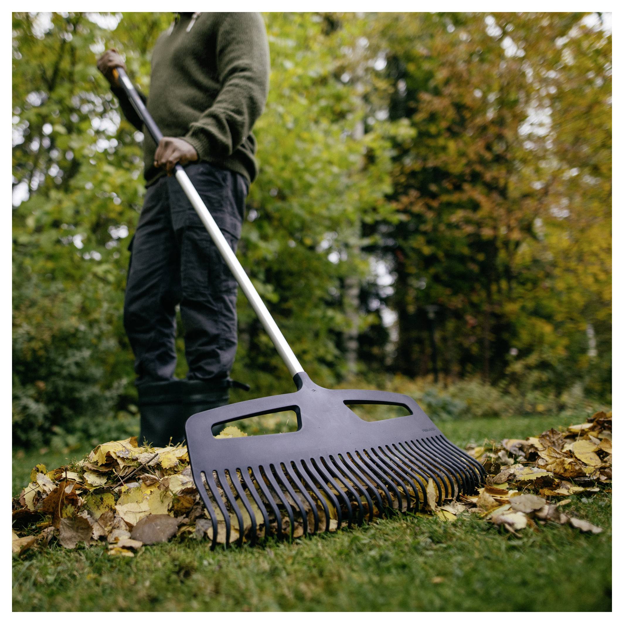 Person, die mit einem breiten Gartenrechen gefallenes Laub in einem Hof zusammenharkt.