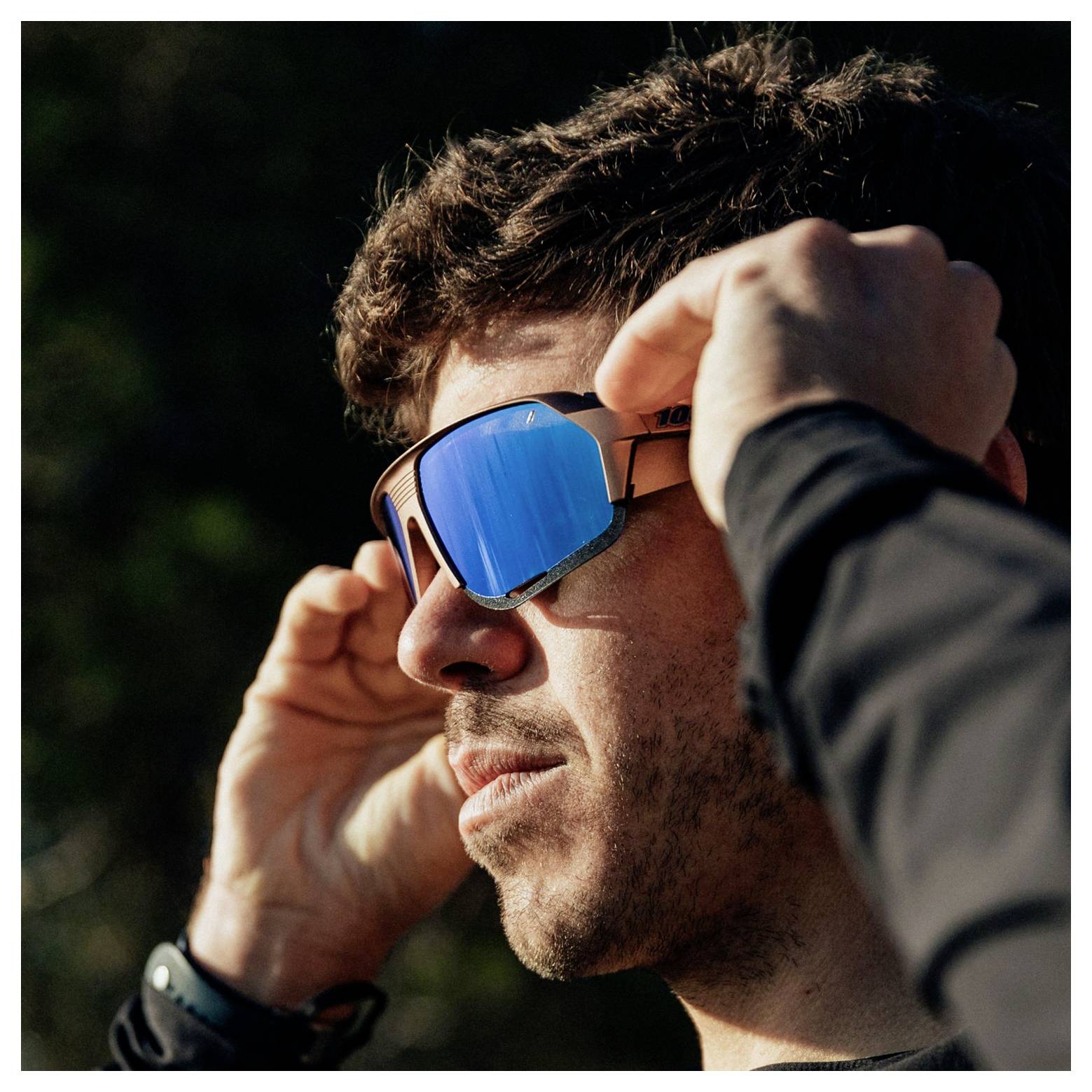 Nahaufnahme eines Mannes, der draußen bei hellem Sonnenlicht eine blaue verspiegelte Sonnenbrille anpasst.