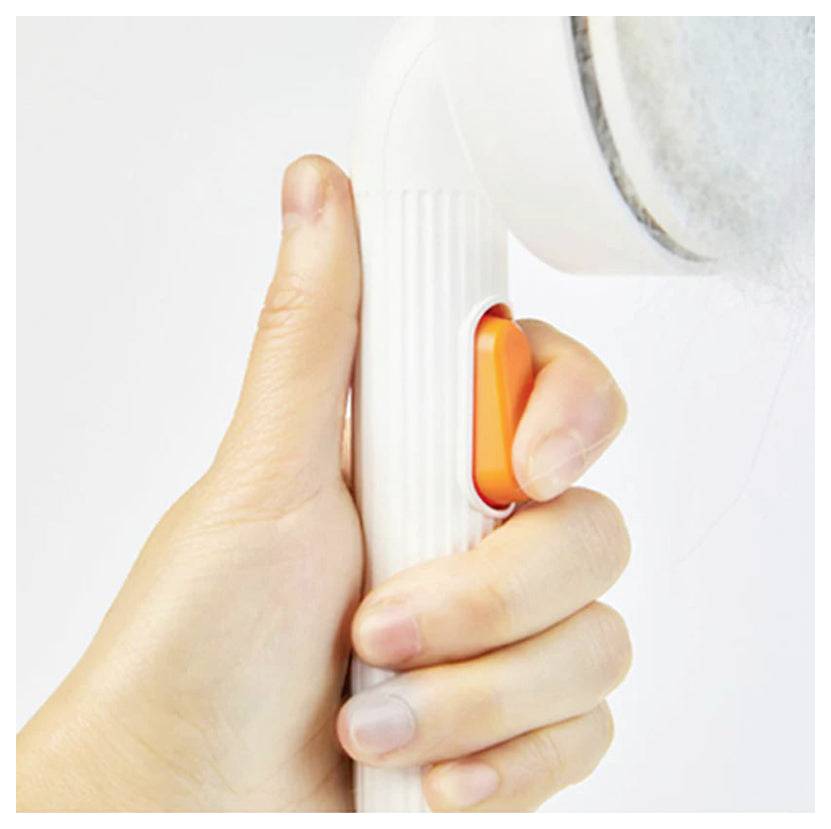 Nahaufnahme einer Hand, die ein weißes Gerät hält und einen orangefarbenen Knopf oder Auslöser gegen eine abgerundete weiße Oberfläche drückt.