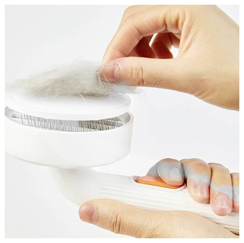 Hände reinigen Flusen aus einer weißen Haarbürste mit einem weißen Reinigungswerkzeug mit orangefarbenem Griff.