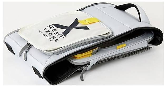 Grauer zusammenklappbarer Reiserucksack mit gelben Akzenten, teilweise geöffnet und gepackt dargestellt; die Vordertasche trägt die Aufschrift „BREEZE X-ZONE
