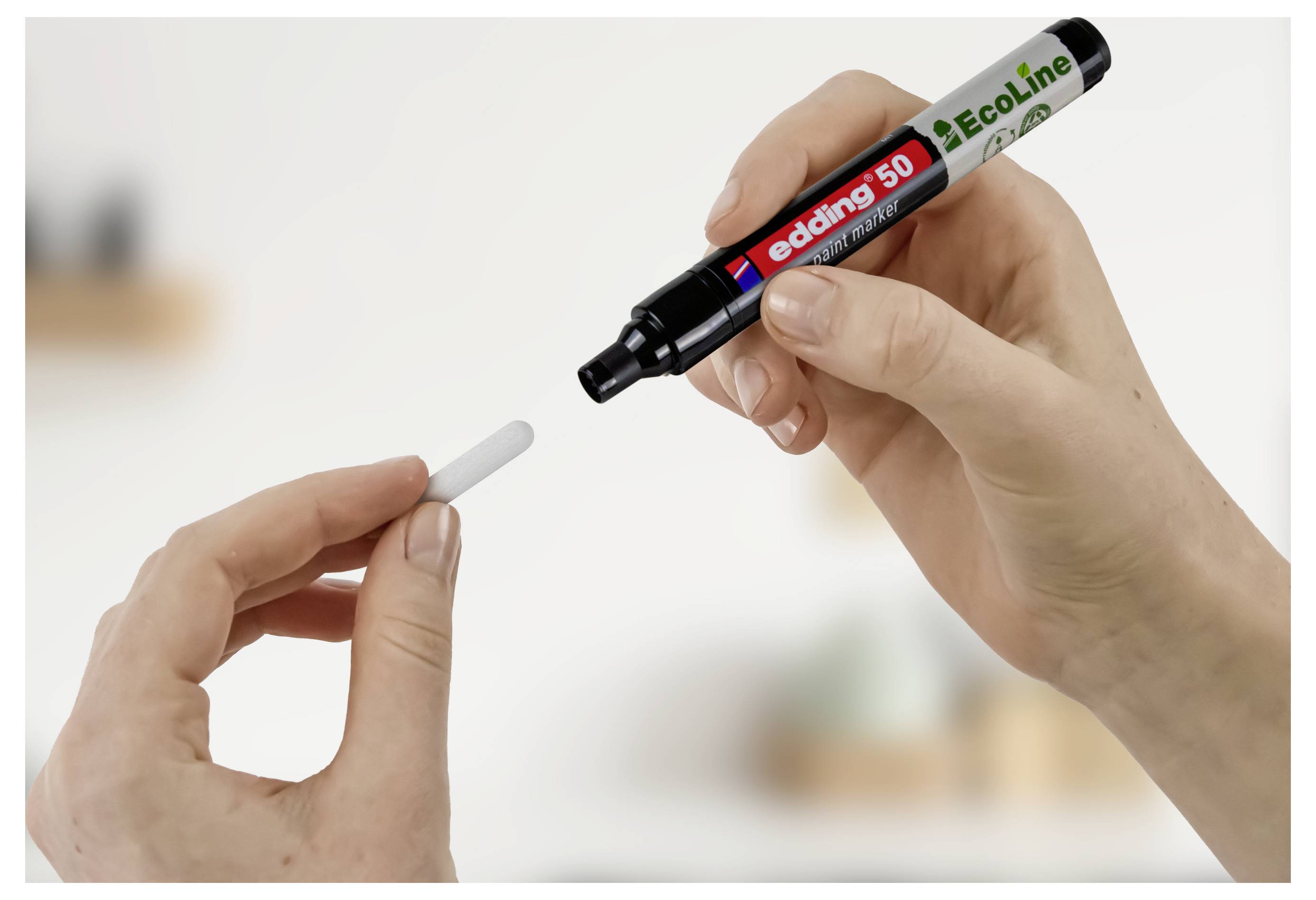 Hände halten einen schwarzen Edding 50 EcoLine Marker über einer kleinen weißen Spitze und zeigen den Stift und seine austauschbare Schreibspitze.