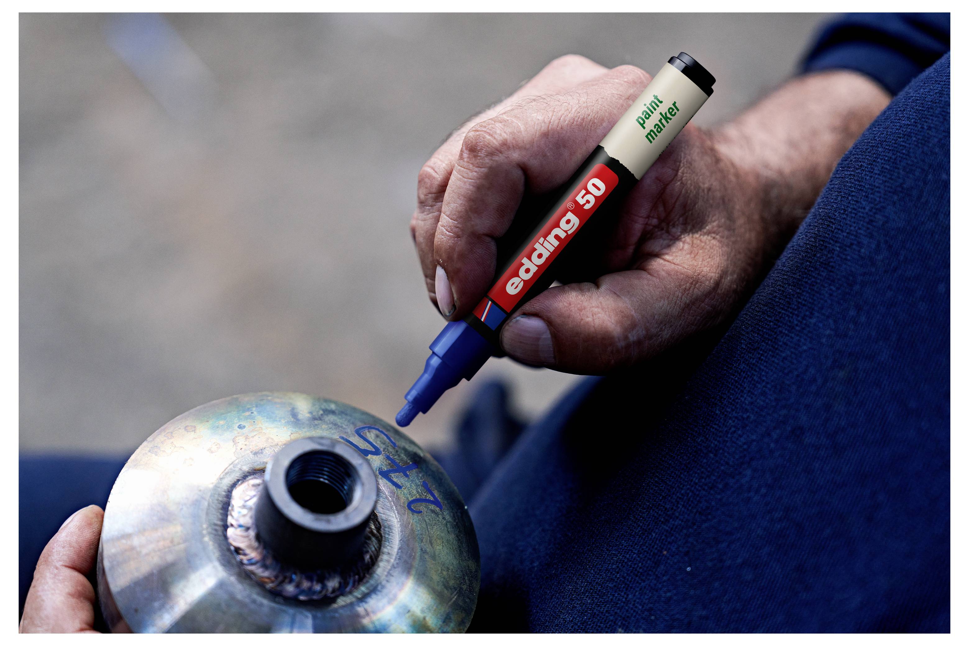 Nahaufnahme einer Person, die ein Metallteil mit einem blauen Lackmarker markiert, wahrscheinlich zur Überprüfung oder Montagekennzeichnung.