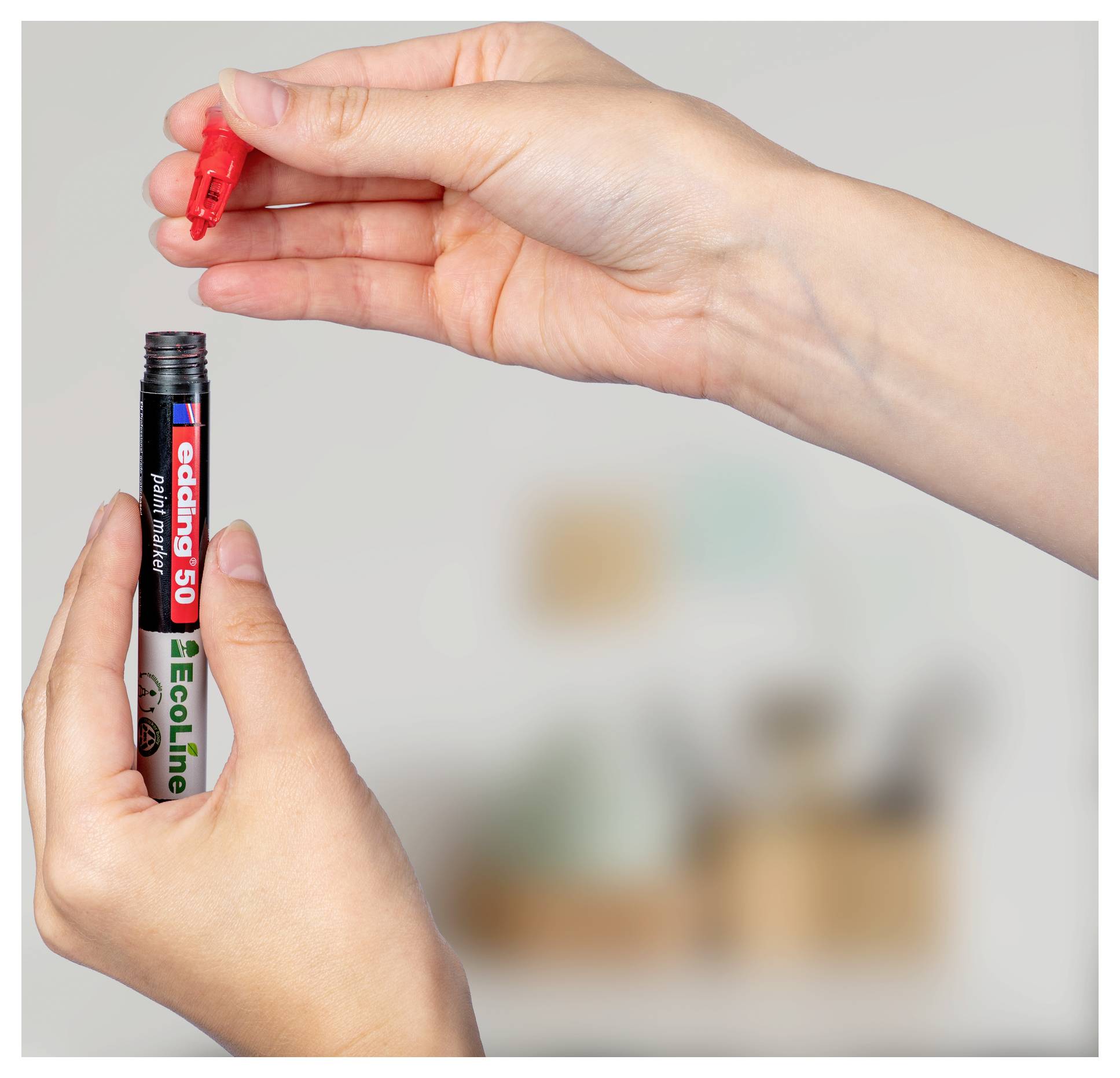 Hände öffnen eine rote Markerkäppchen über einem schwarzen edding 500 Ecoline Stift, bereit zum Gebrauch.