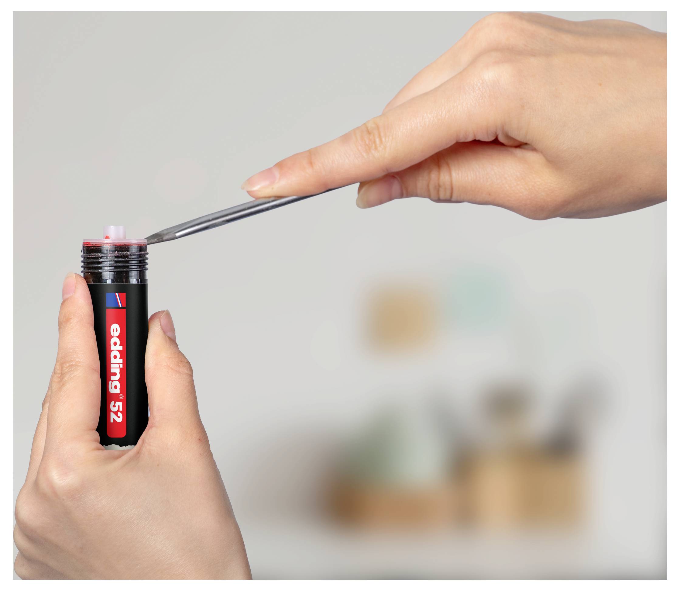 Hände halten einen Edding 52 Marker, während eine Pinzette eine Spitze in den offenen Schaft einführt und zeigt dabei die Reparatur oder den Zusammenbau eines Stifts.
