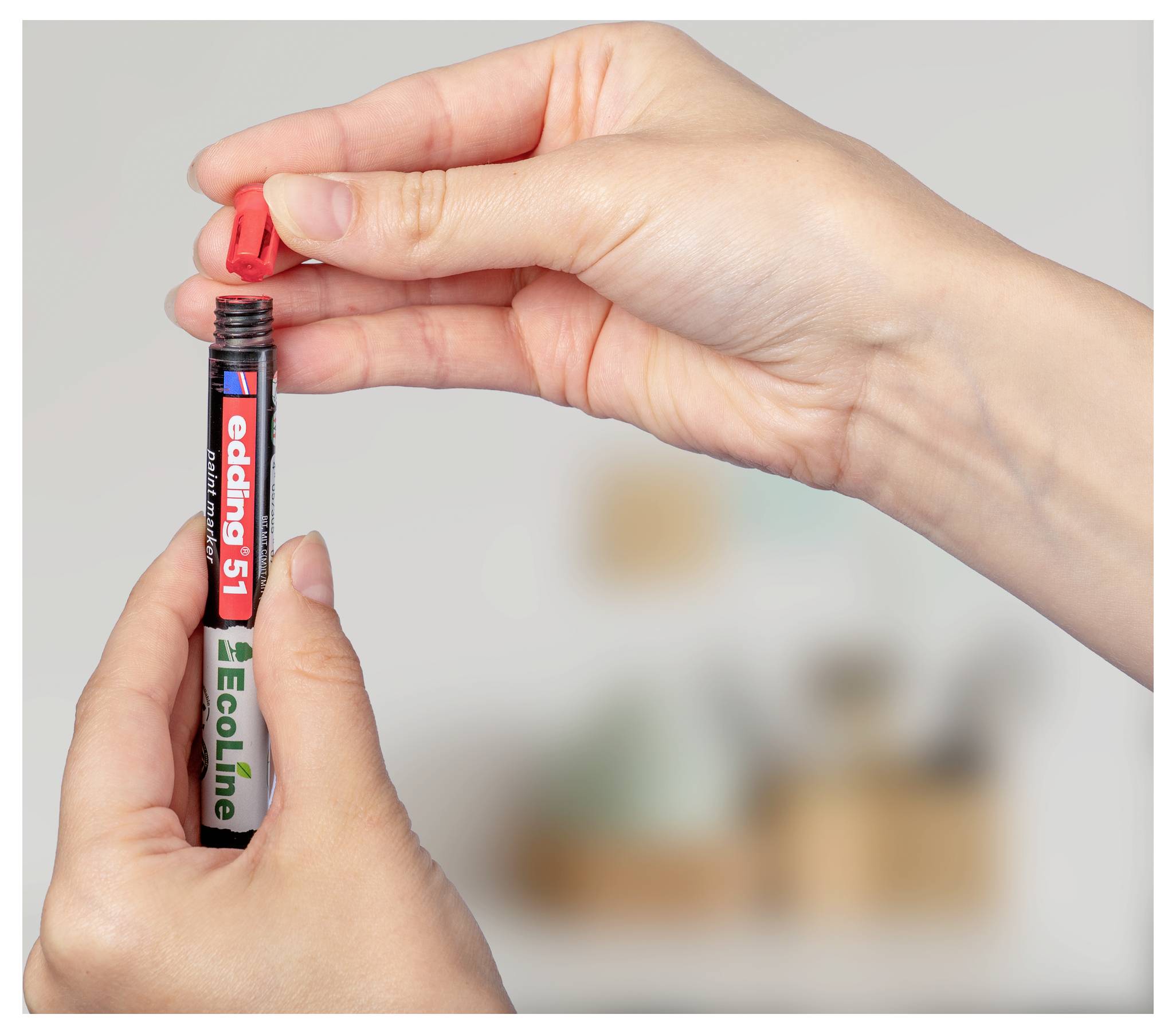 Hände öffnen eine rote Kappe von einem stiftähnlichen Marker mit der Aufschrift 
