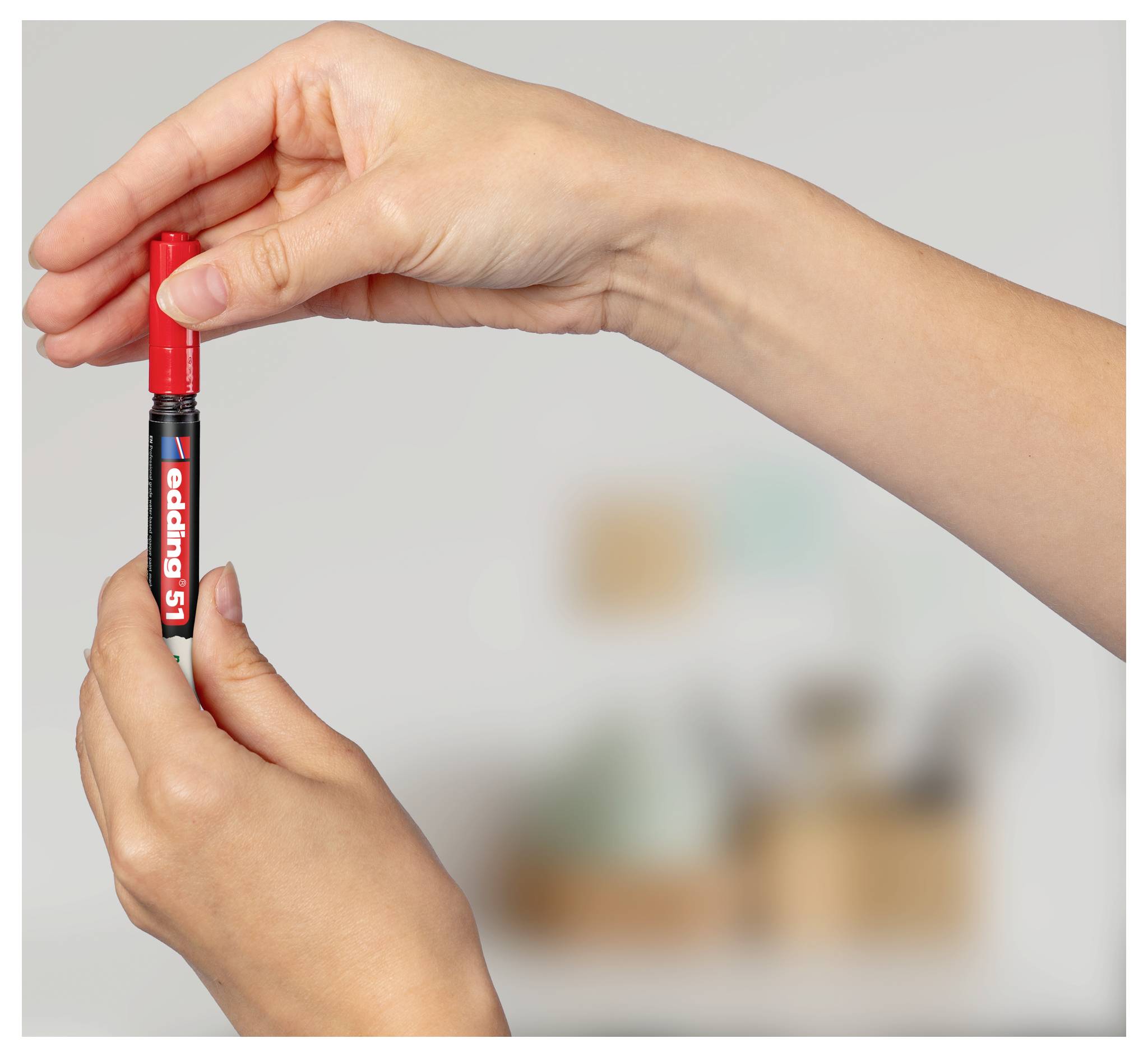 Hände, die einen roten Markierungsstift aufrecht halten, wobei die Kappe entfernt wird.
