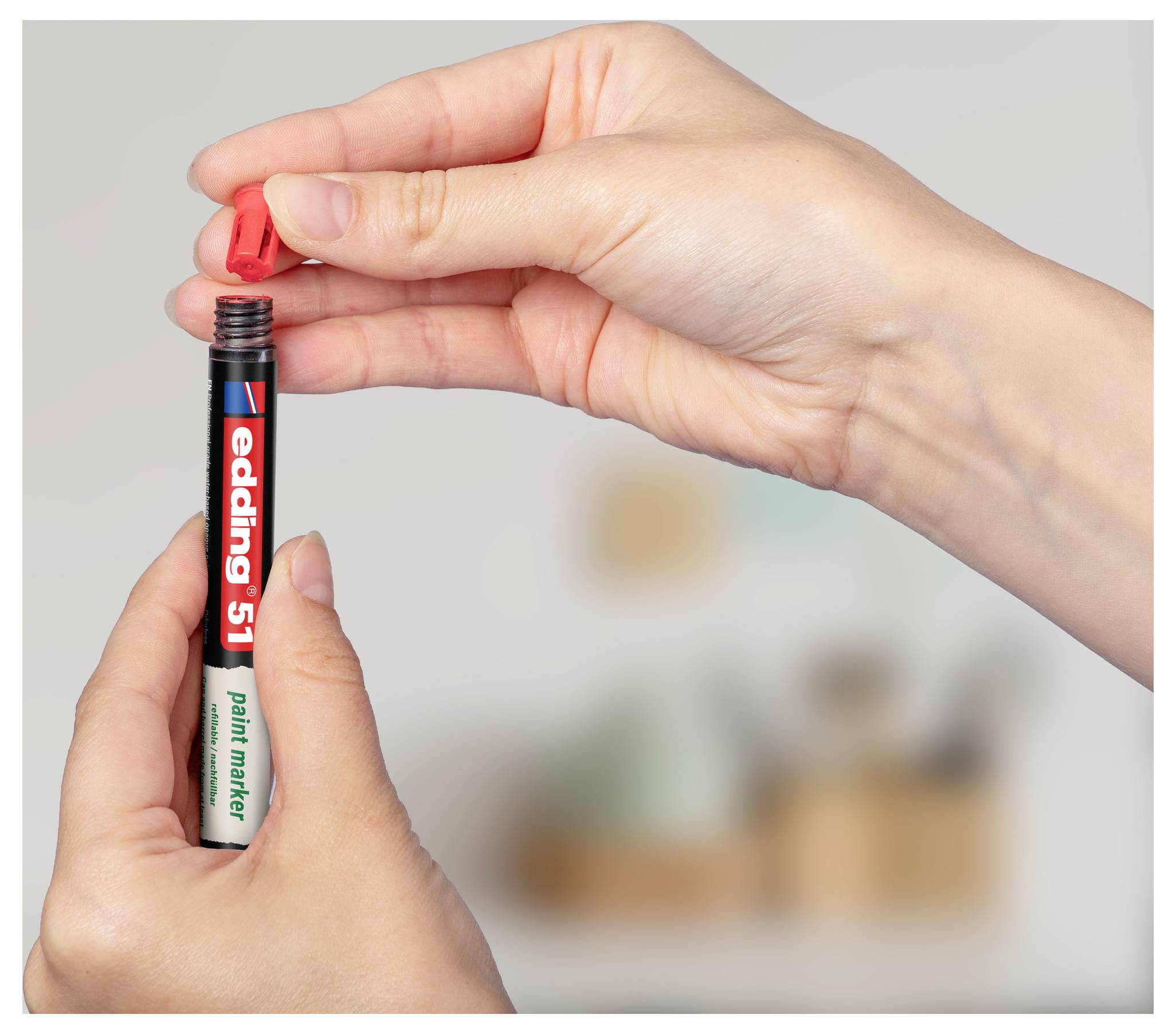 Hände, die einen roten Lackmarker öffnen, zeigen die Stiftspitze und das Label „edding 51" vor einem unscharfen Hintergrund.