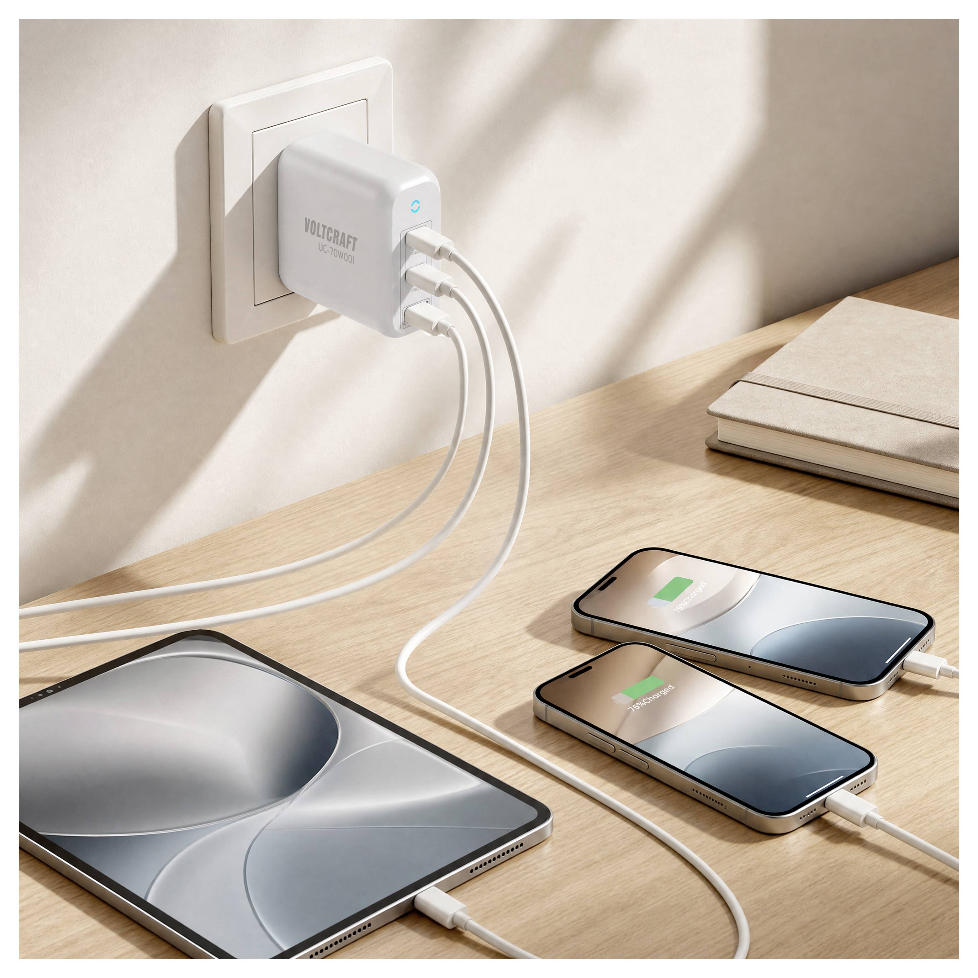 Ladestation auf einem Schreibtisch mit einem Wandladegerät, das über weiße Kabel ein Tablet und zwei Smartphones mit Strom versorgt