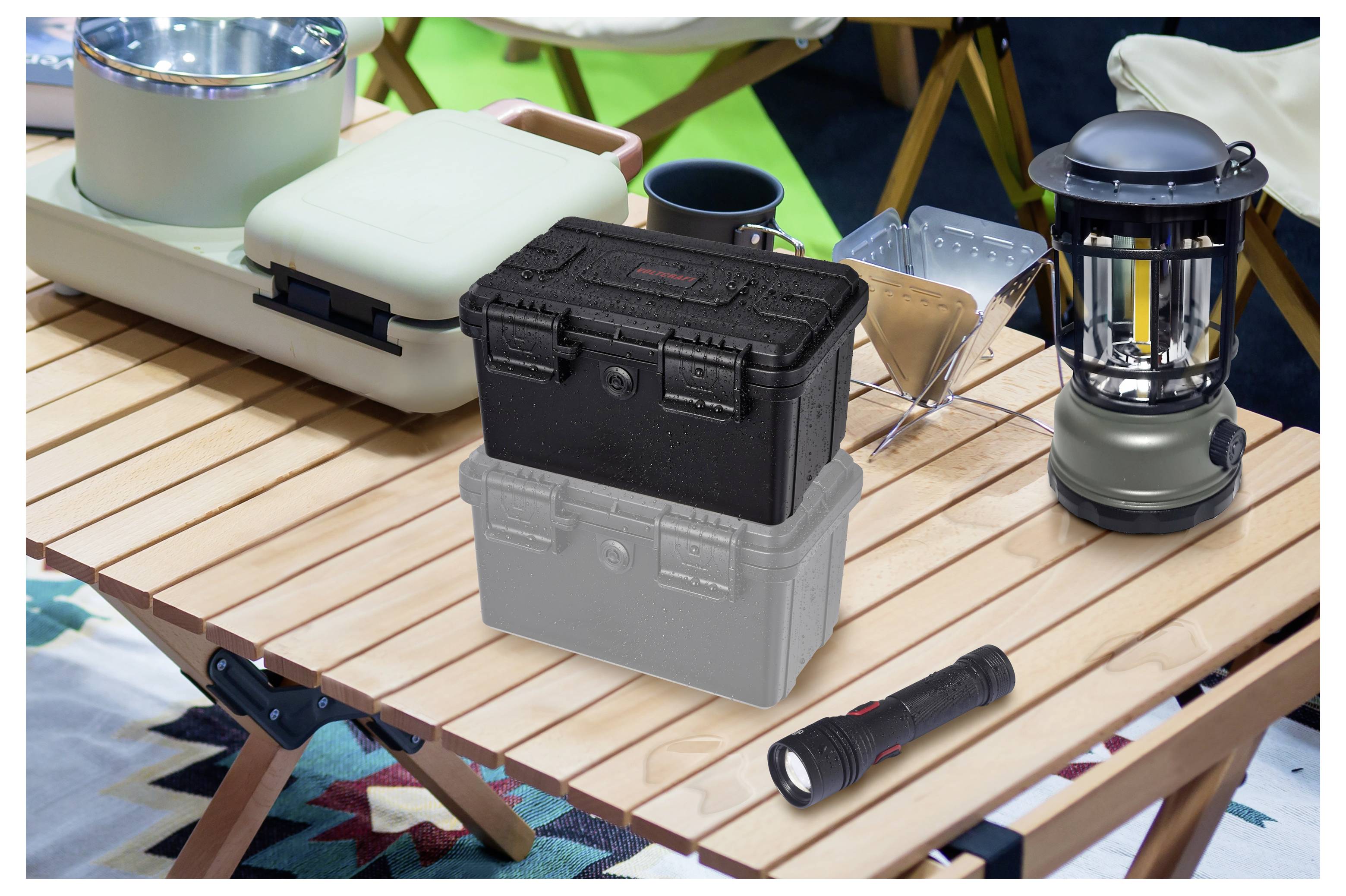 Schwarze und graue robuste Aufbewahrungskästen auf einem lamellerten Holz-Campingtisch, mit einer Laterne und einer Taschenlampe in der Nähe.