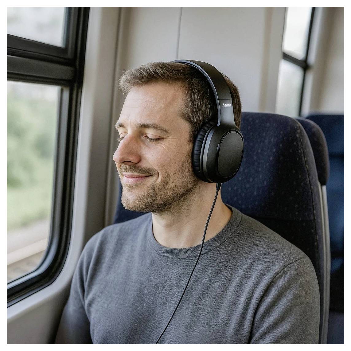 Ein Mann mit Over-Ear-Kopfhörern sitzt mit geschlossenen Augen am Zugfenster und wirkt entspannt und konzentriert auf das Hören von Audio.