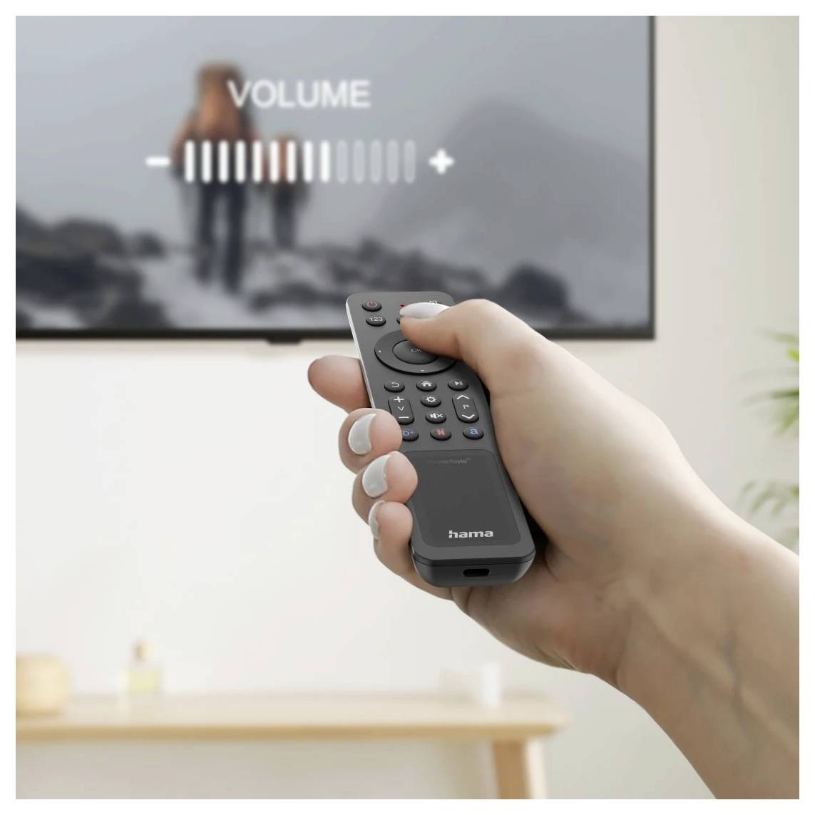 Hand hält eine Fernbedienung, während die Lautstärke auf einem Fernsehbildschirm eingestellt wird, auf dem „VOLUME