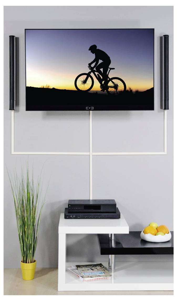 Flachbildfernseher mit Schattenriss eines Radfahrers bei Sonnenuntergang über einem weißen Medienständer mit Lautsprechern, einer Pflanze und einer Schüssel mit Orangen.