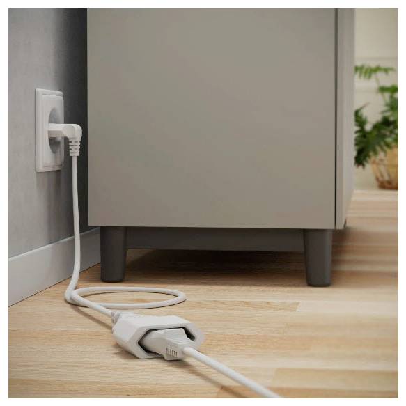 Stromkabel, das in eine Steckdose an einer Wand angeschlossen ist, auf einem Boden mit dem Kabel, das vor einem Schrank aufgerollt ist und eine häusliche Stromverbindung zeigt.