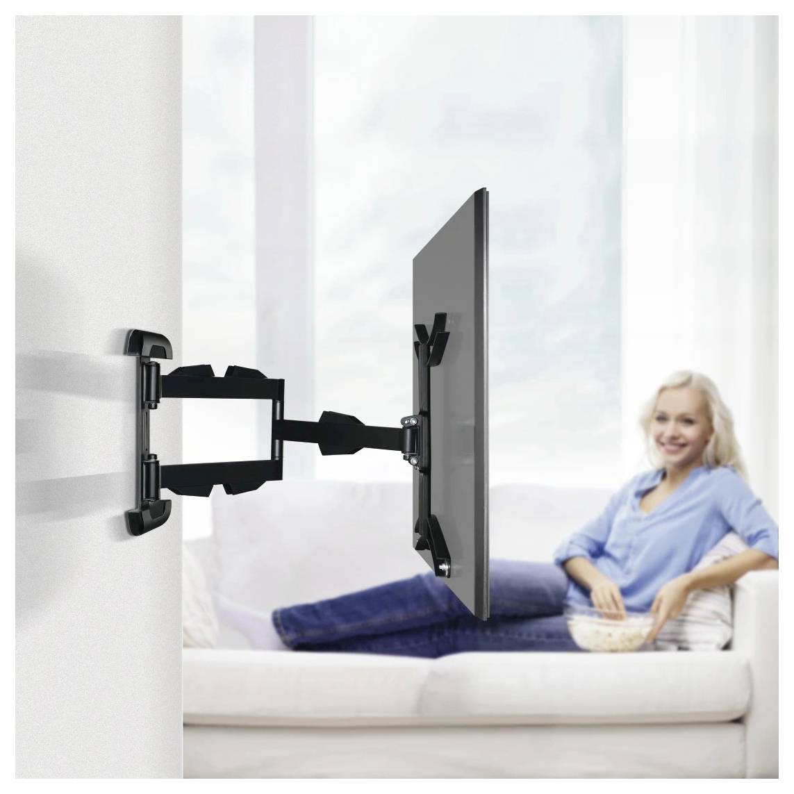 Ein Fernseher, der an einer Wand mit einem ausziehbaren Arm befestigt ist, während eine Frau sich im Hintergrund auf einem Sofa entspannt.