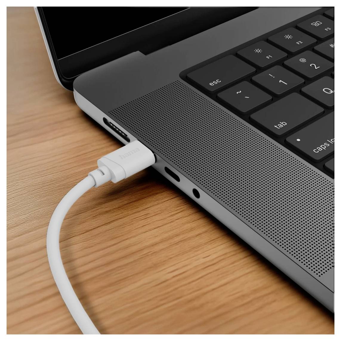 White USB-C cable plugged into the side of a laptop on a wooden desk, showing a charging or data connection.