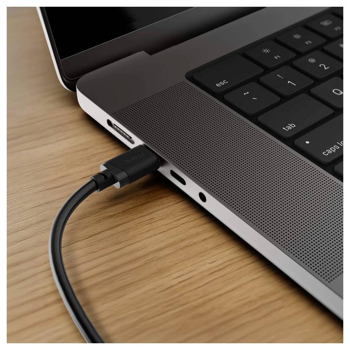 Nahaufnahme der Seite eines Laptops mit einem USB-C-Kabel, das in den Anschluss auf einem Holzschreibtisch eingesteckt ist.