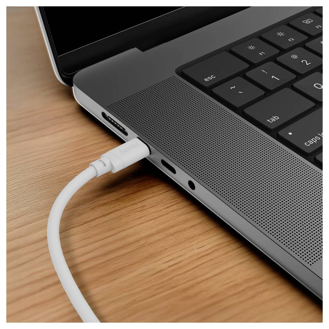 Nahaufnahme eines Laptop-Seitenports mit einem weißen Kabel, das auf einem Holzschreibtisch eingesteckt ist.