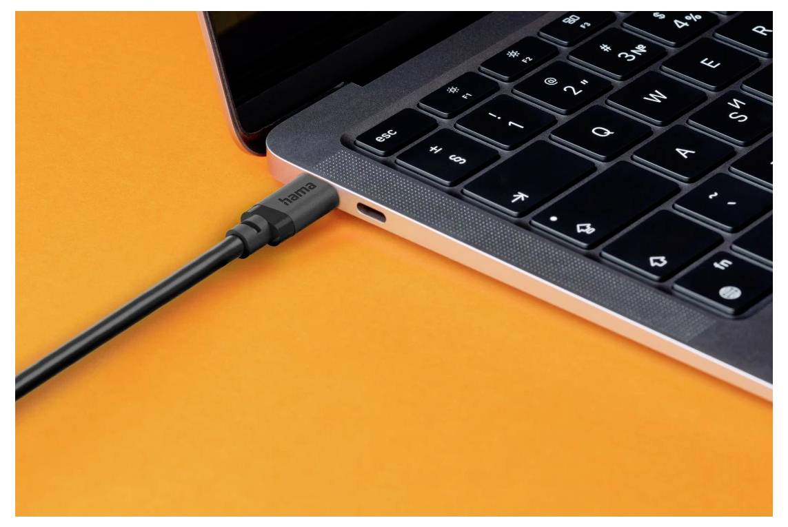 Nahaufnahme der Seite eines Laptops mit einem in einen USB-C-Anschluss eingesteckten Kabel auf orangefarbenem Hintergrund.
