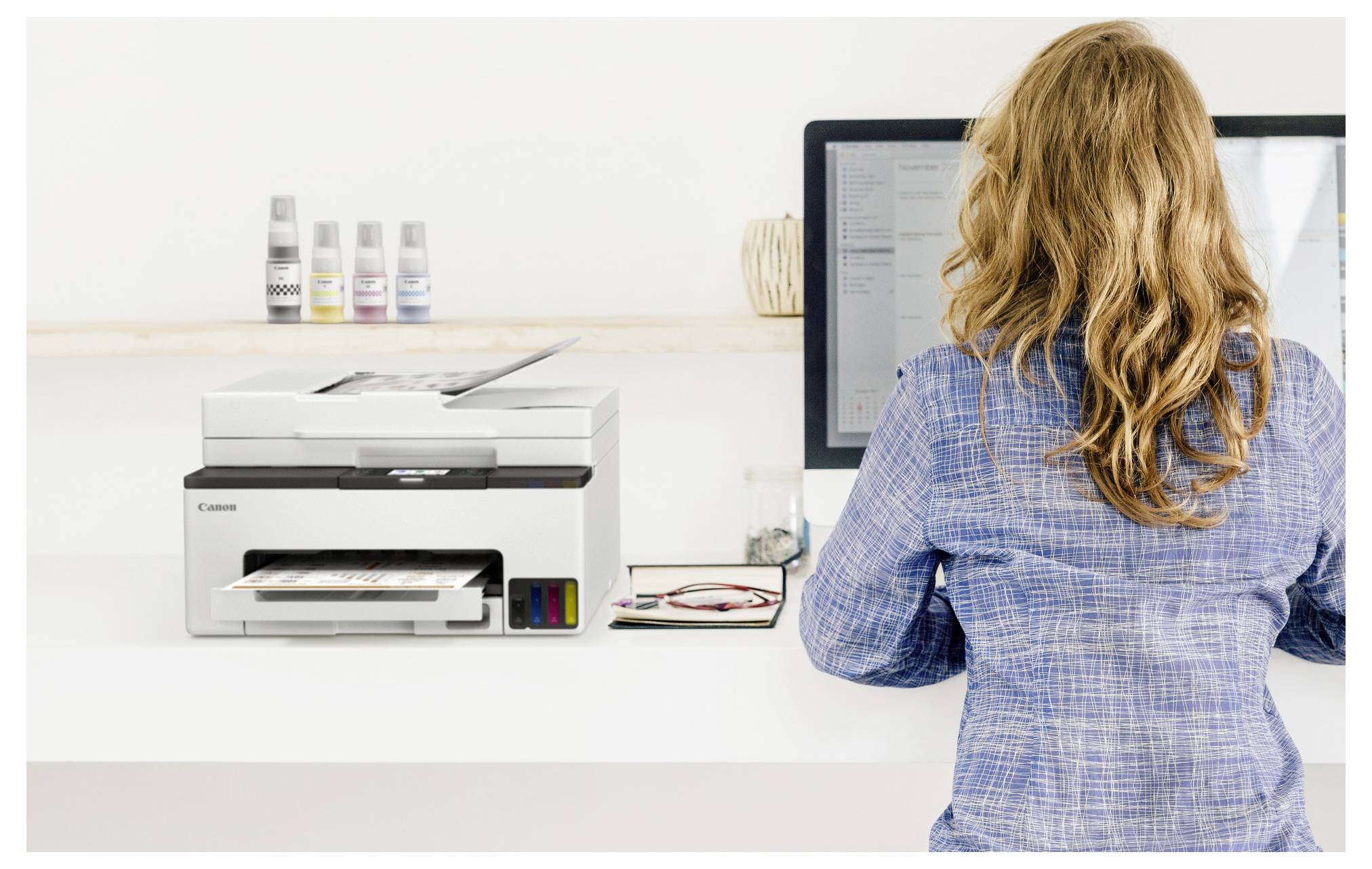 Frau, die neben einem Canon-Drucker an einem Computer in einem Büro oder Druckladen steht und ein Dokument auf dem Bildschirm ansieht.