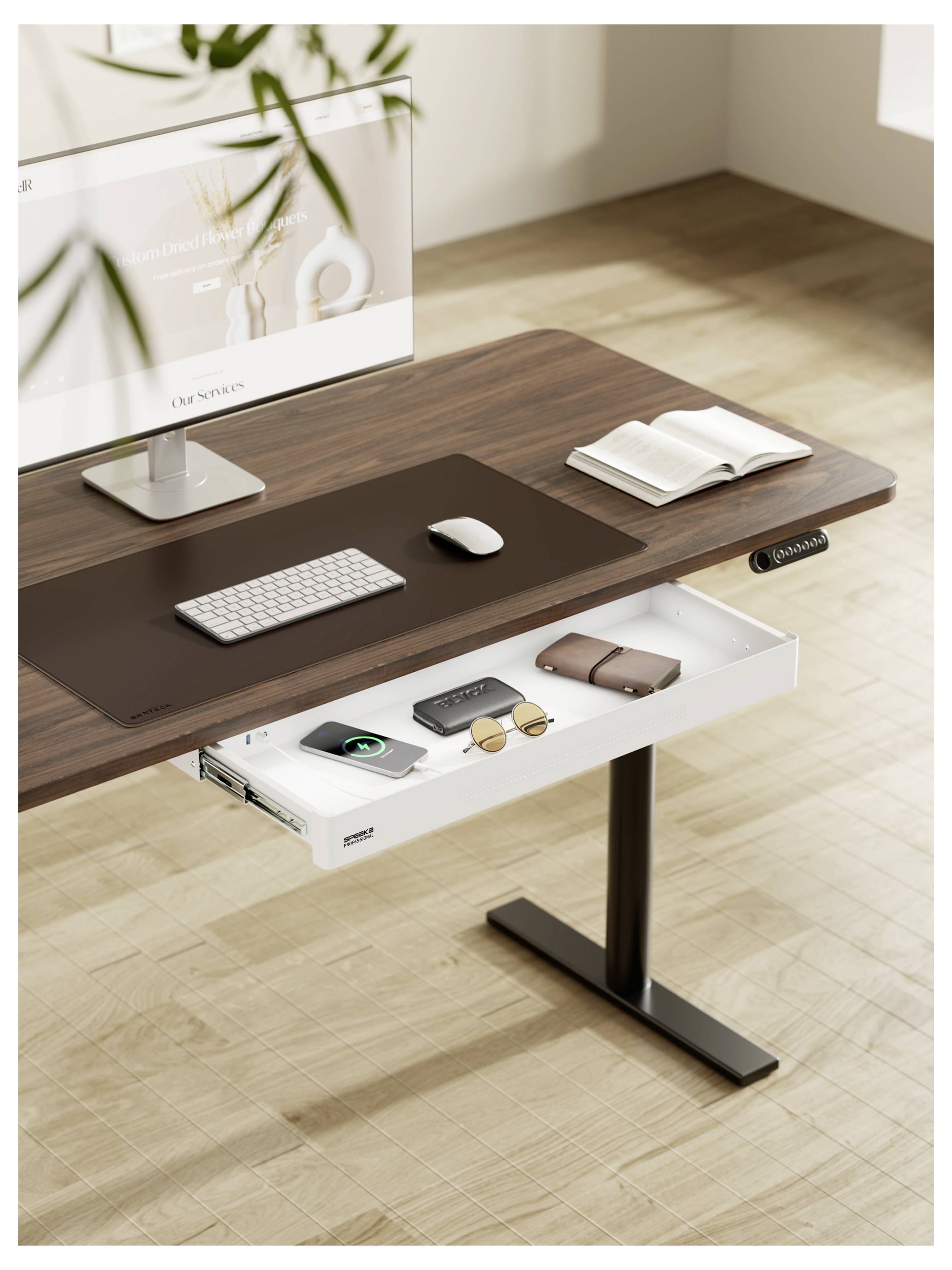 Moderner Stehschreibtisch mit Monitor, Tastatur, Maus, aufgeschlagenem Notizbuch und einer ausziehbaren Schublade mit Zubehör auf hellem Holzboden.