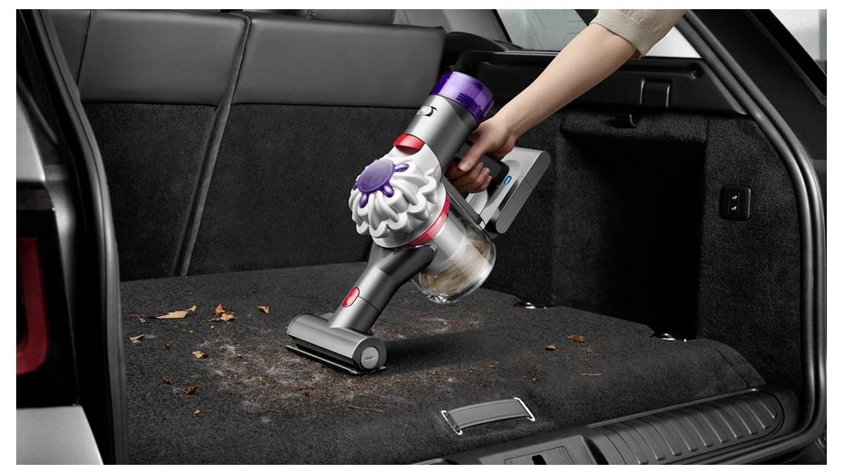 Tragbarer kabelloser Staubsauger reinigt Schmutz und Blätter aus einem Autokofferraum-Teppich.