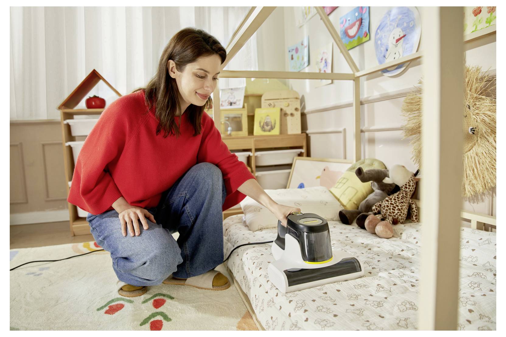 Frau staubsaugt ein Kinderbett in einem hellen Schlafzimmer, mit Kuscheltieren und Spielzimmerdekoration im Hintergrund.