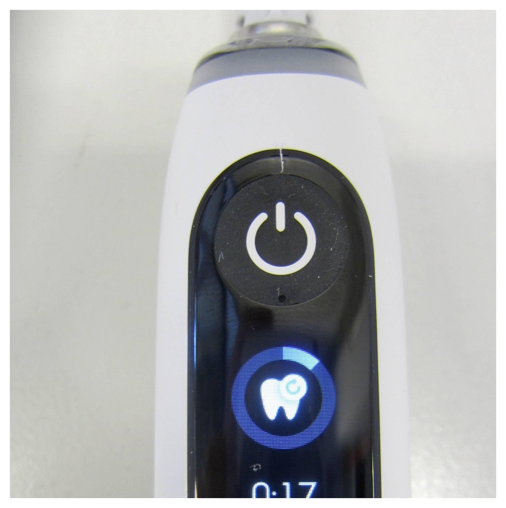 Nahaufnahme eines Elektrozahnbürsten-Griffs mit der Ein-/Ausschalttaste und einem blau beleuchteten Zahnbürsten-Modus-Symbol.